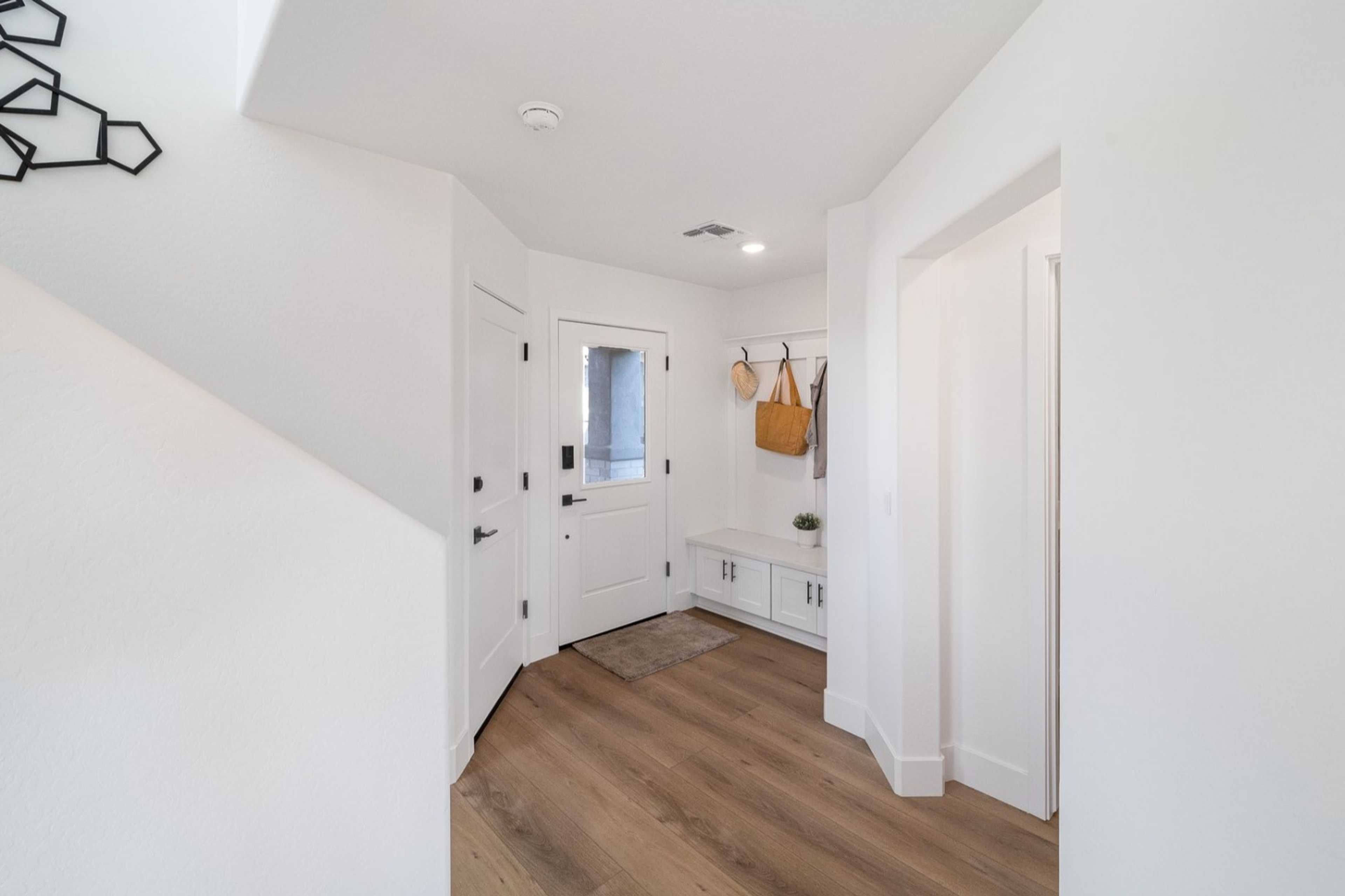 Spacious entryway in The Wilmington B with white walls, hardwood floors, built-in bench, coat hooks, and geometric wall art
