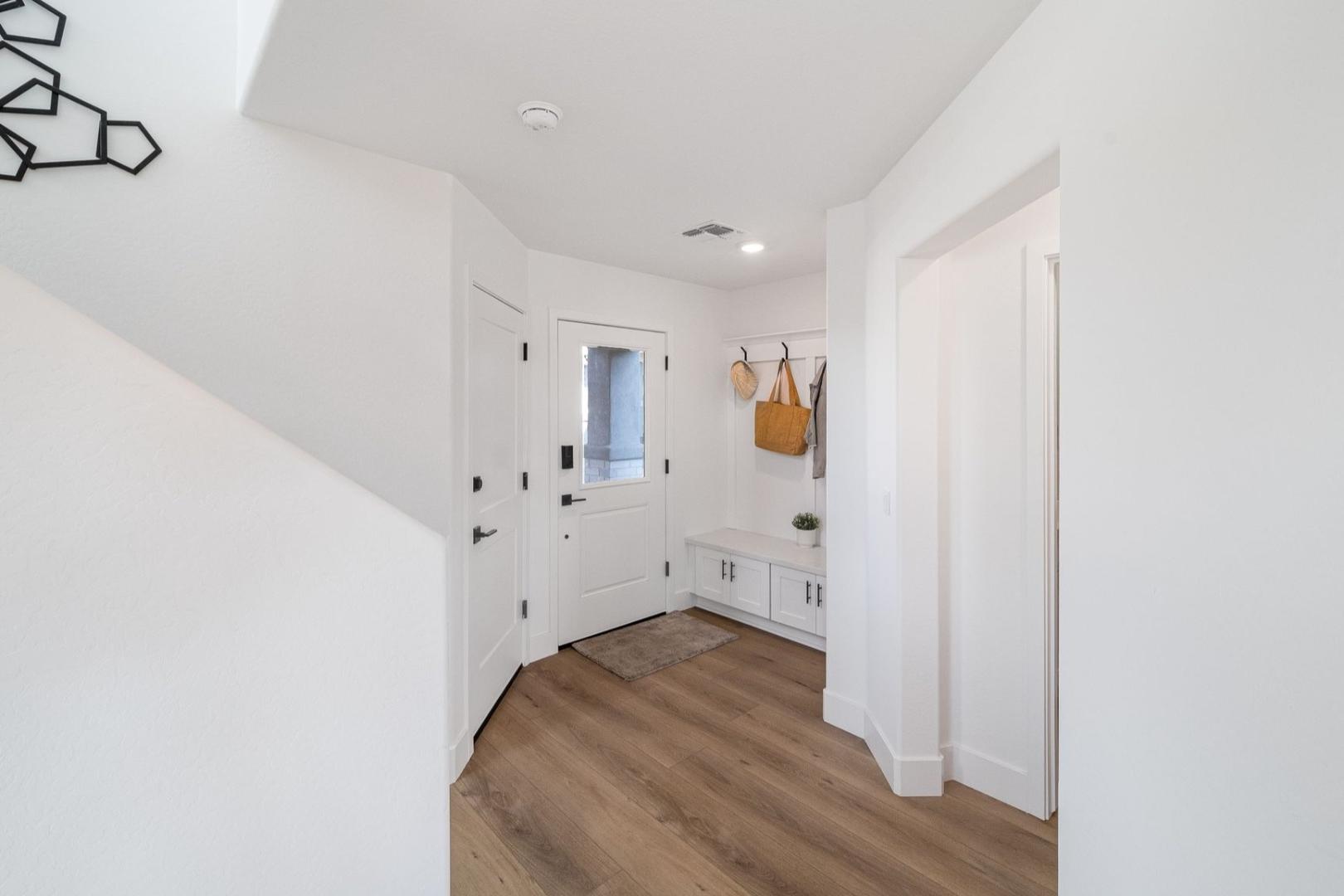 Spacious Wilmington entryway with white paneled door, coat hooks, cushioned bench, hardwood floors, and geometric wall art