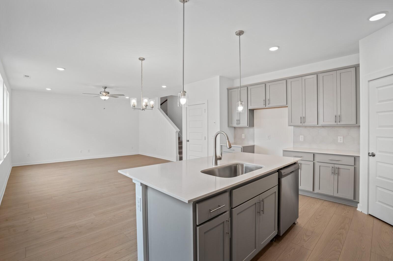 Open-concept kitchen with gray cabinetry and island in The Logan B floor plan at Calista Farms, White House, Tennessee.