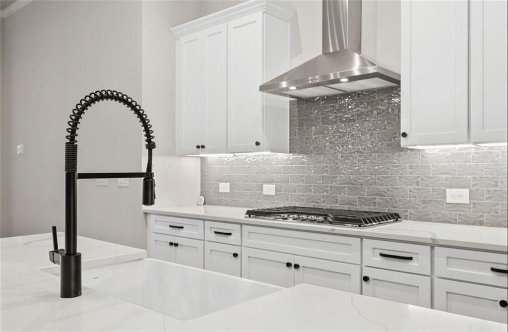 Modern kitchen featuring white shaker cabinets, quartz countertops, black pull-down faucet, stainless hood in Davidson Homes The Seaside A, Woodstock GA