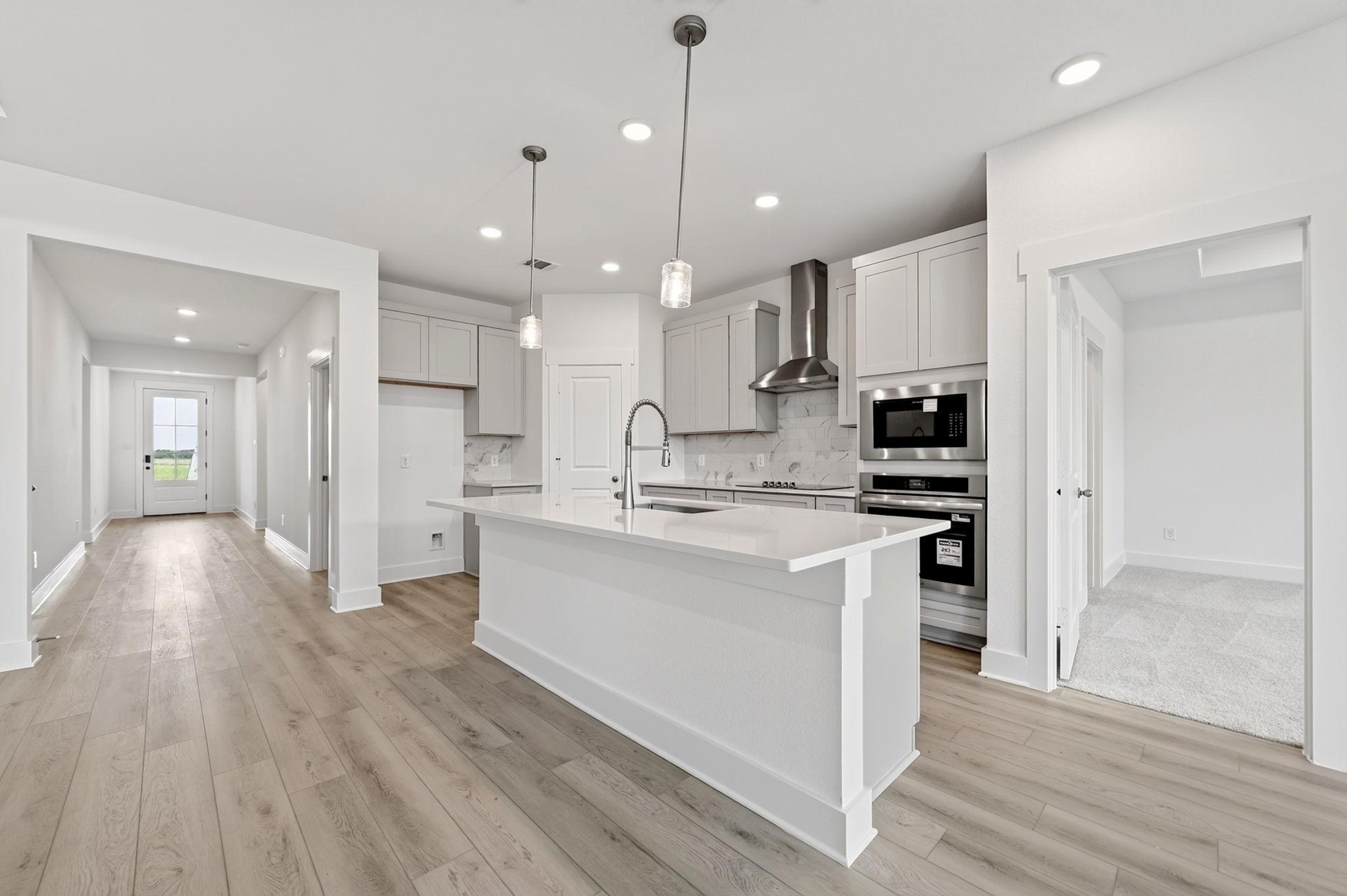 Modern kitchen with white island, gray shaker cabinets, marble backsplash, and stainless appliances in Davidson Homes The Holly F plan