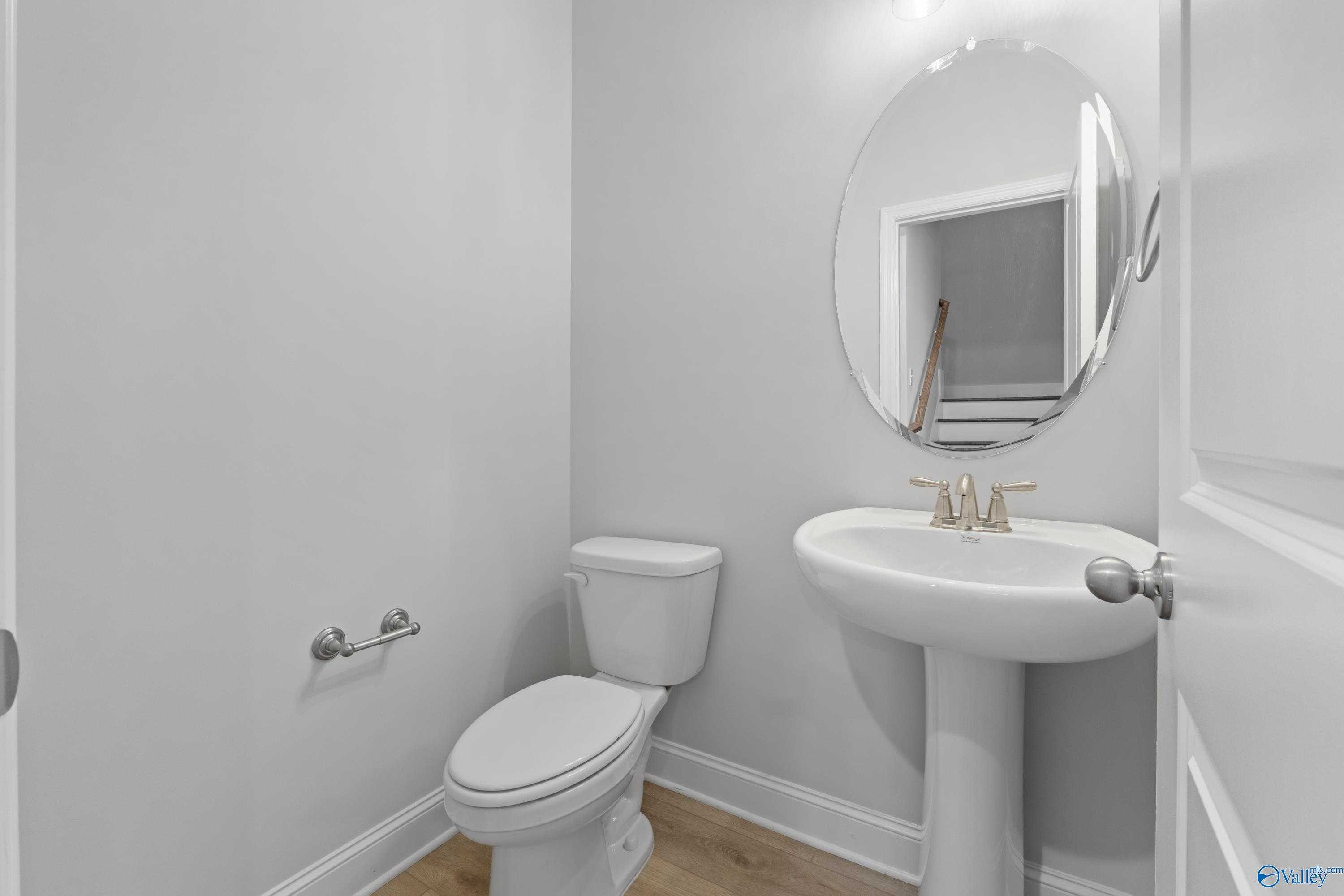 Modern powder room with pedestal sink, round mirror, and white toilet in Davidson Homes The Rockford B with Bonus, Toney, Alabama