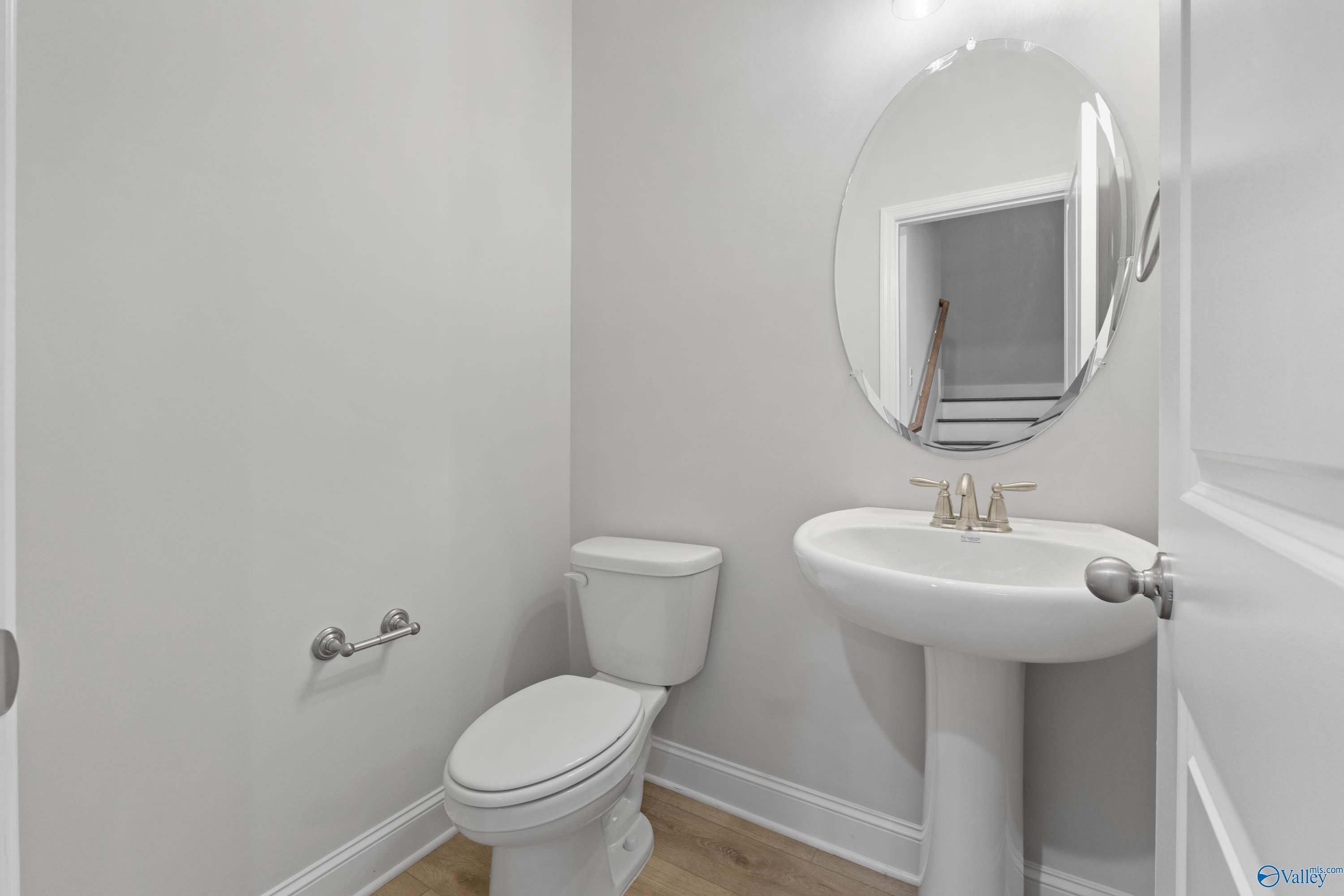 Elegant powder room with pedestal sink, gold faucet, round mirror and toilet in Davidson Homes The Rockford B with Bonus, Toney, Alabama