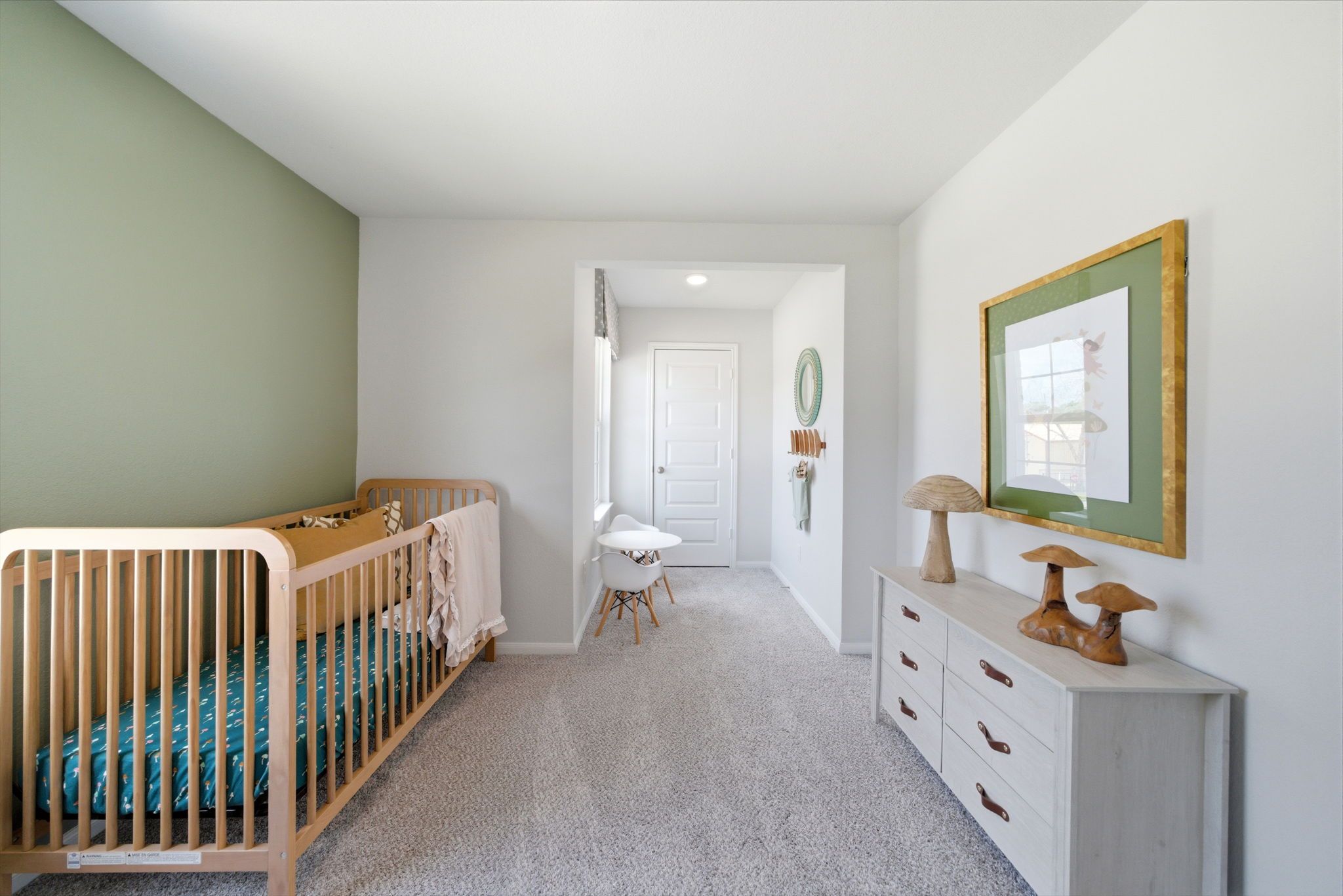 Cozy nursery at Caney Creek Place in Conroe TX by Davidson Homes with wooden crib, green accent wall, white dresser and desk
