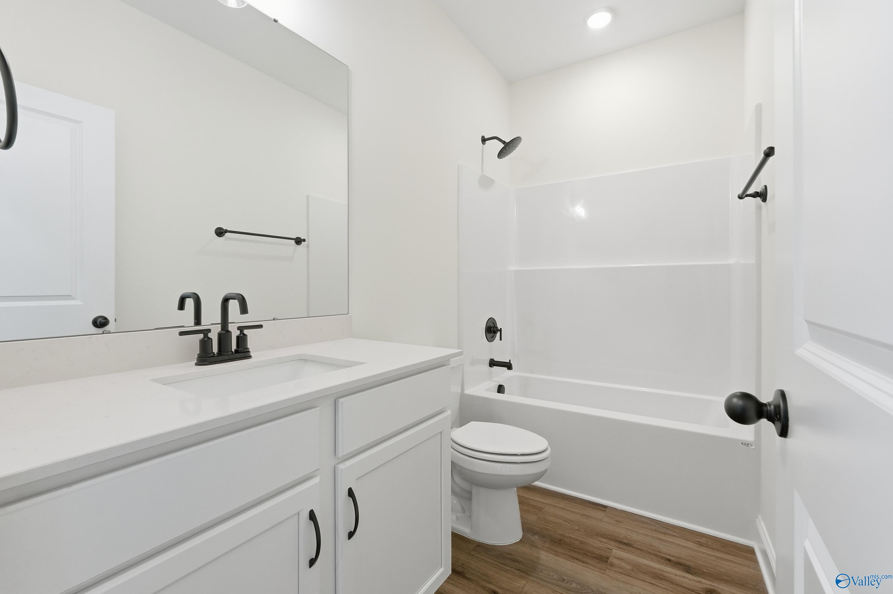 Modern white bathroom with double vanity, tub-shower combo, and luxury vinyl plank flooring in Davidson Homes The Franklin C, New Market, Alabama