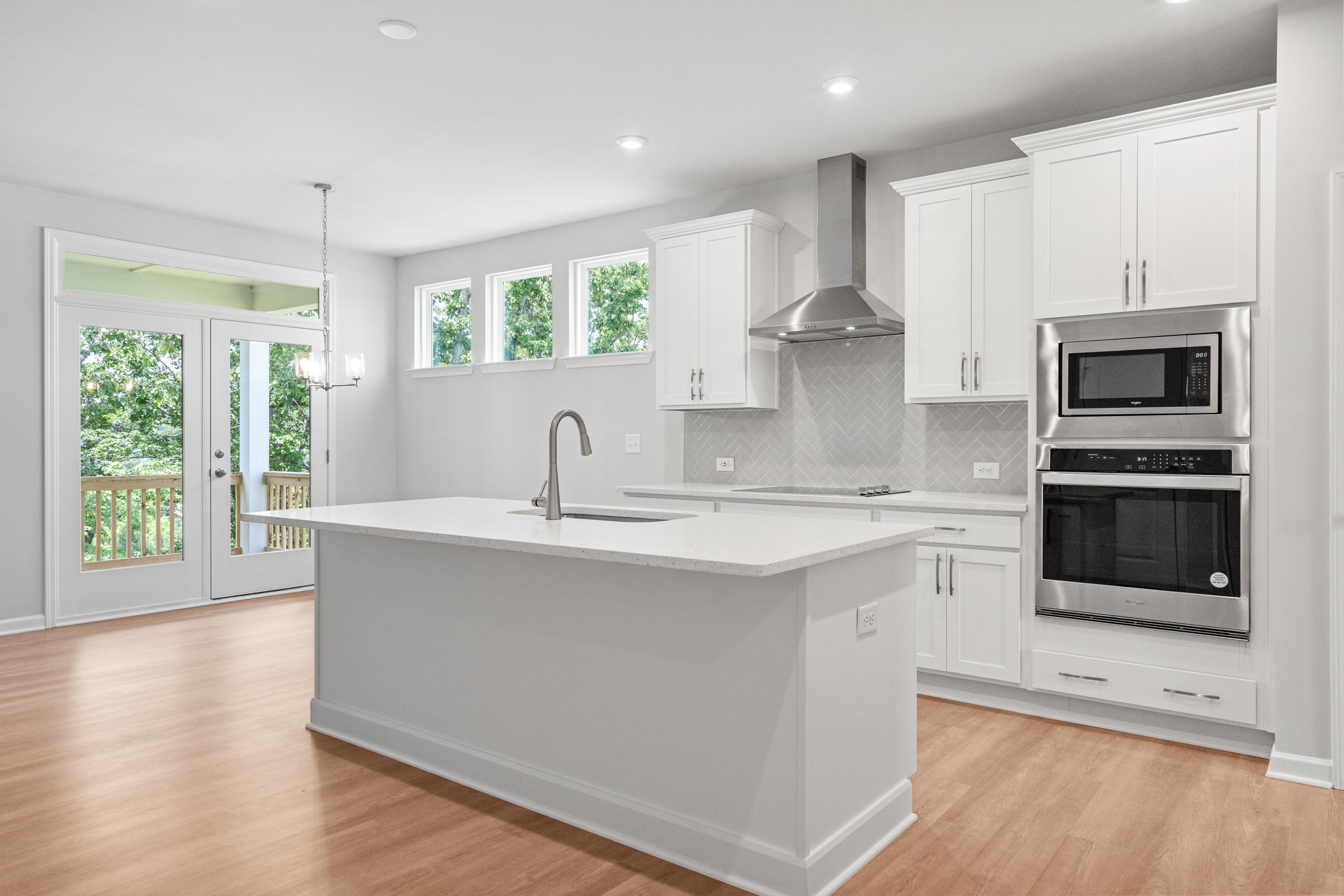 Spacious kitchen in The Ash B at Wehunt Meadows featuring white shaker cabinets, large quartz island, stainless steel double ovens, and French doors to deck