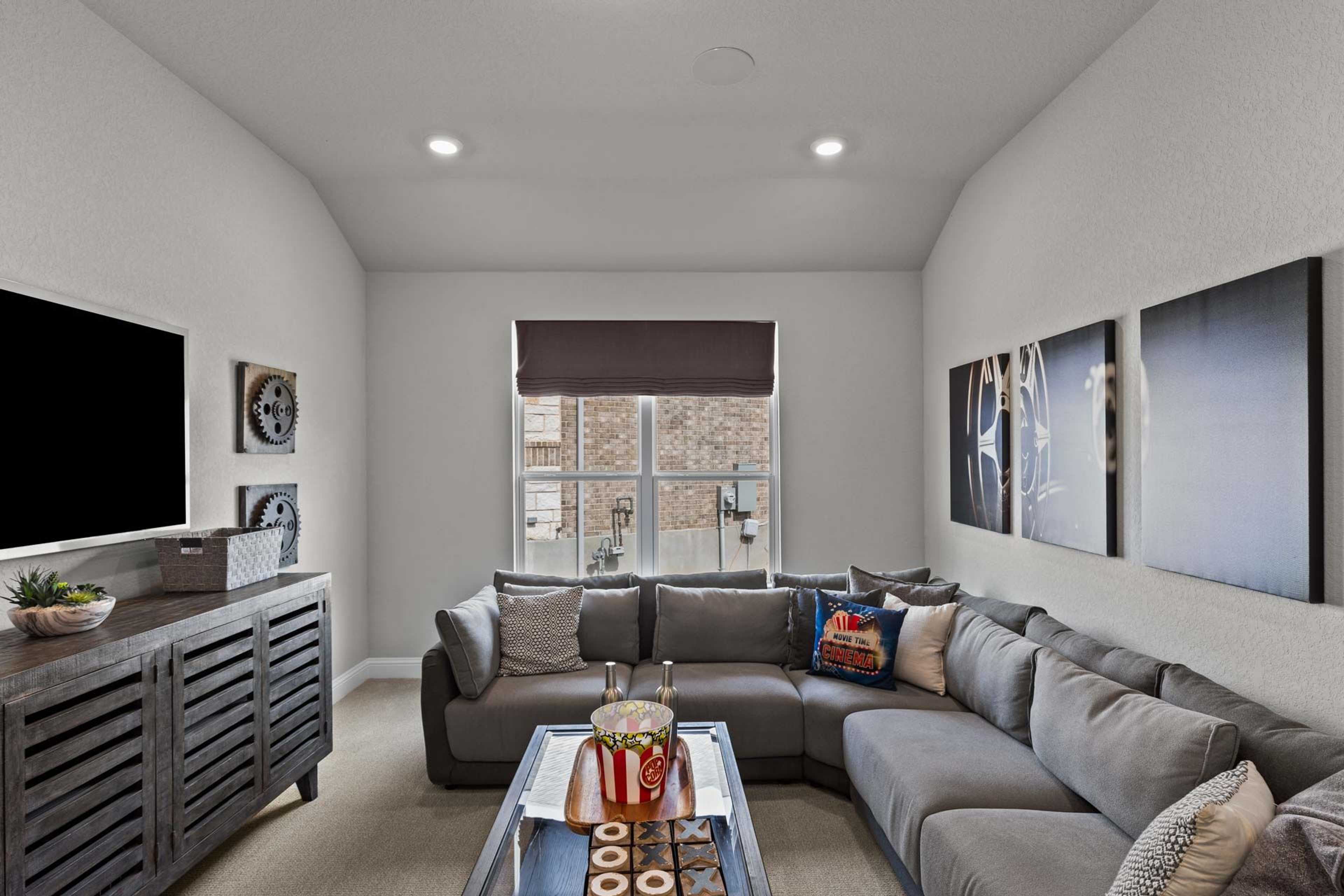 Cozy media room at Ladera in San Antonio TX with L-shaped gray sectional sofa, mounted TV, and arched ceiling