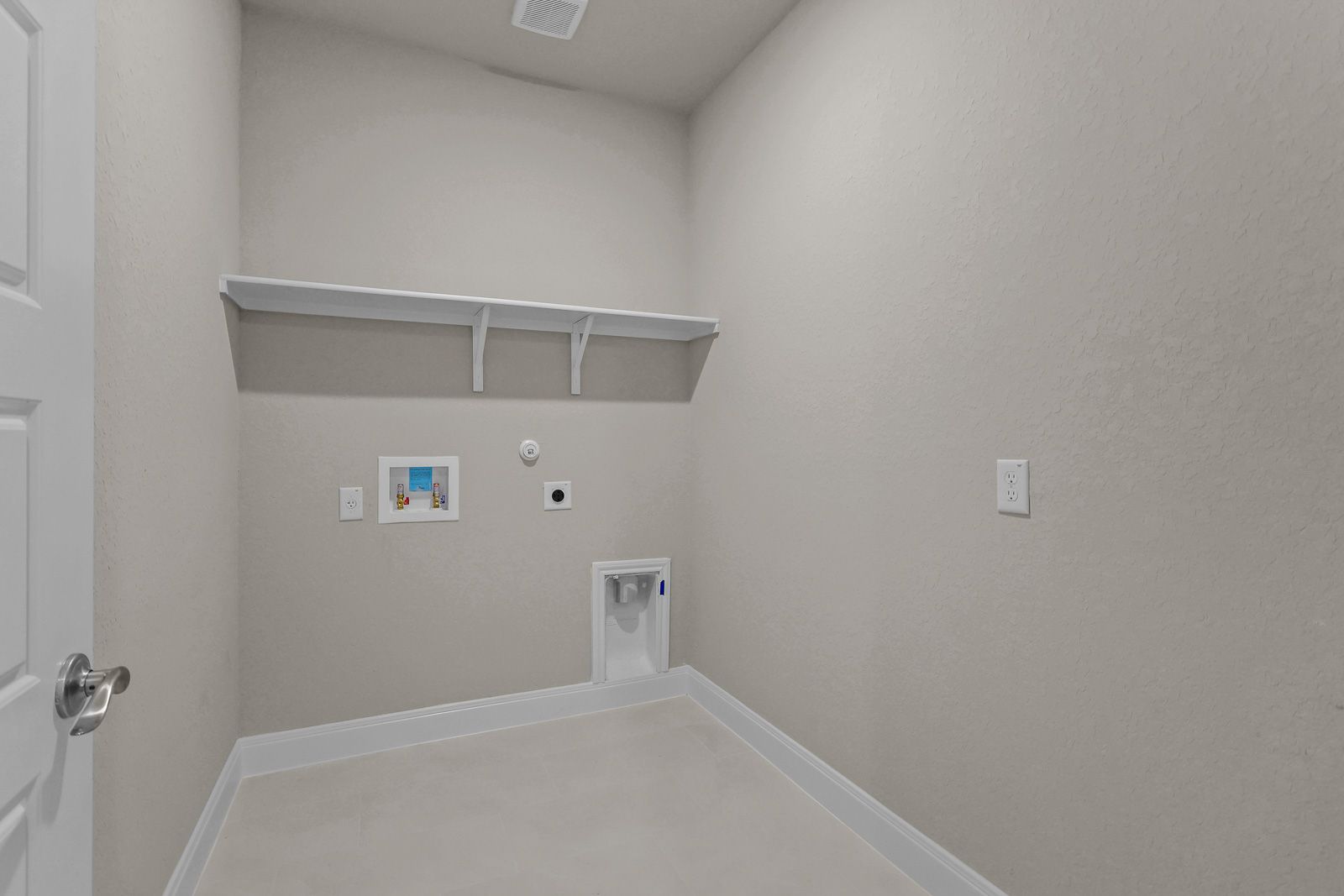 Spacious laundry room in The Jennings G design featuring neutral walls, tile flooring, and built-in storage shelving.