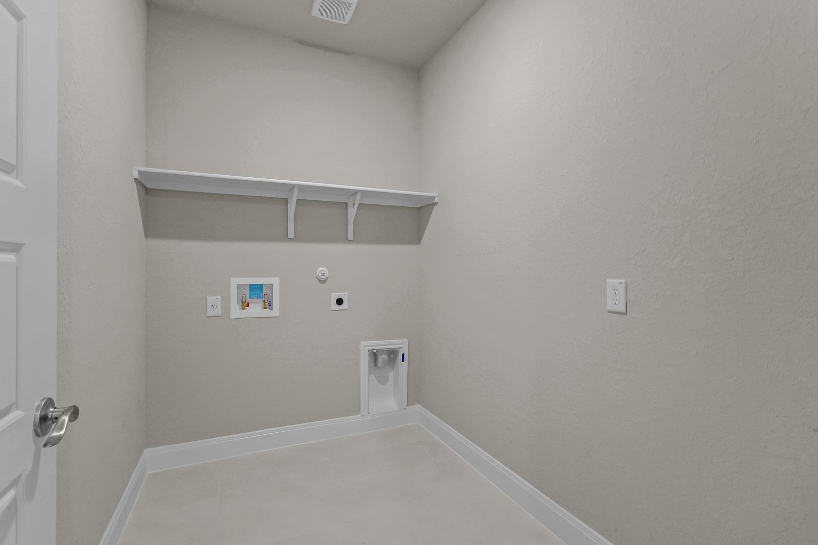 Spacious laundry room in The Jennings G design featuring neutral walls, tile flooring, and built-in storage shelving.