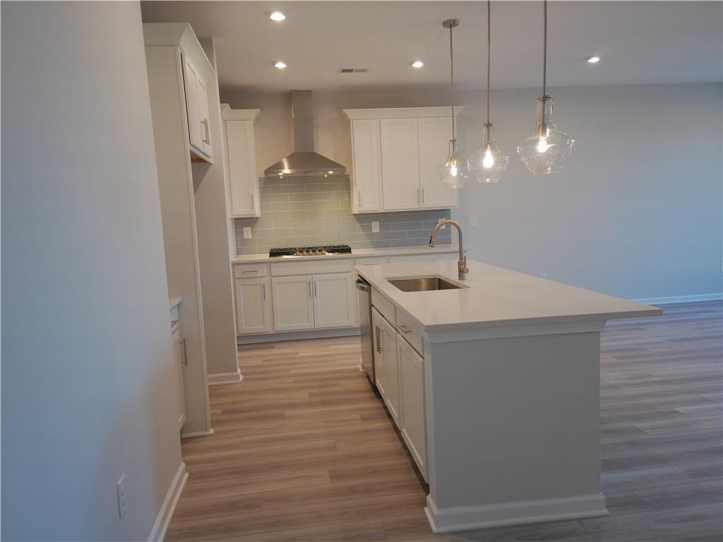 Modern white kitchen with quartz island sink, stainless gas range, subway tile backsplash, and pendant lights in Davidson Homes The Marion C, Winder GA