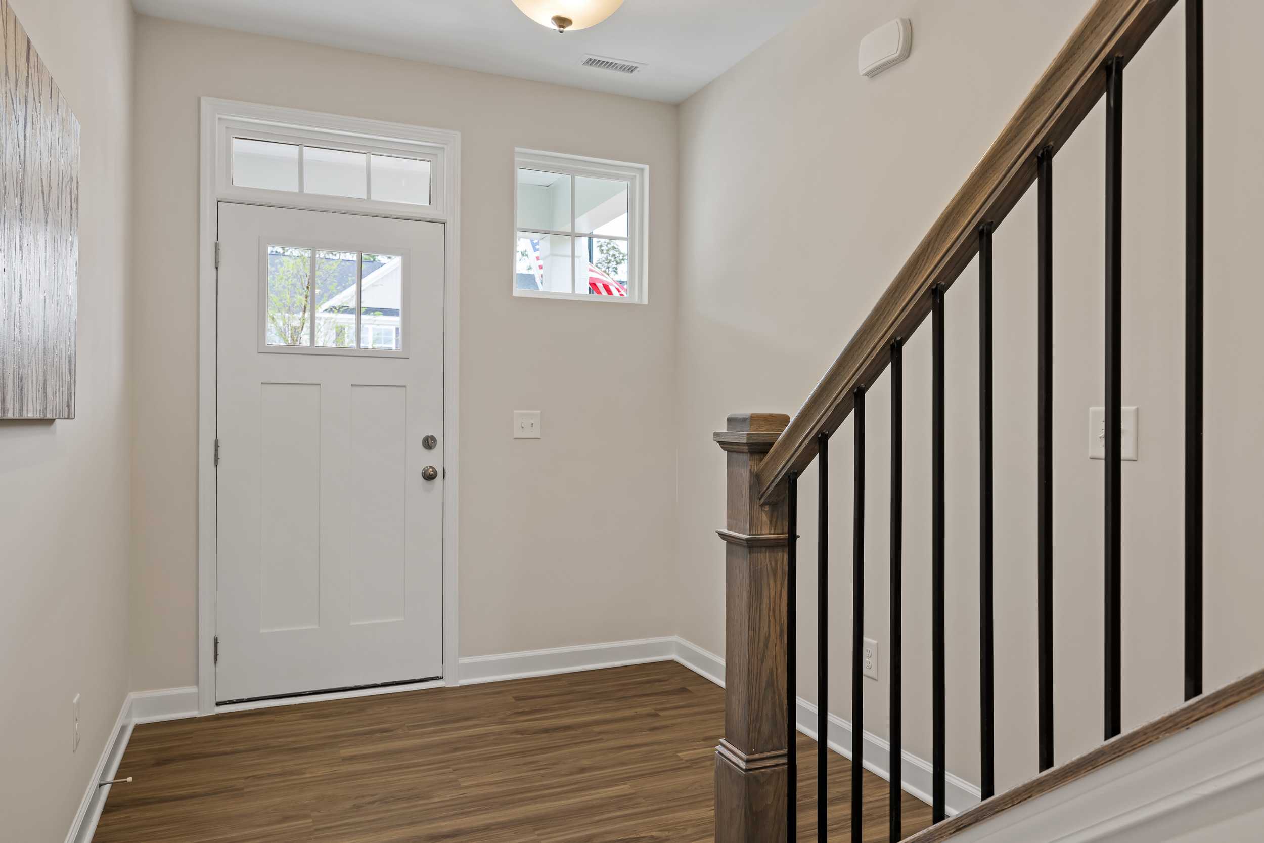 Spacious entry foyer at Gregory Village in Lillington NC with white glass-paneled door, wooden stairs, black railings, and hardwood floors
