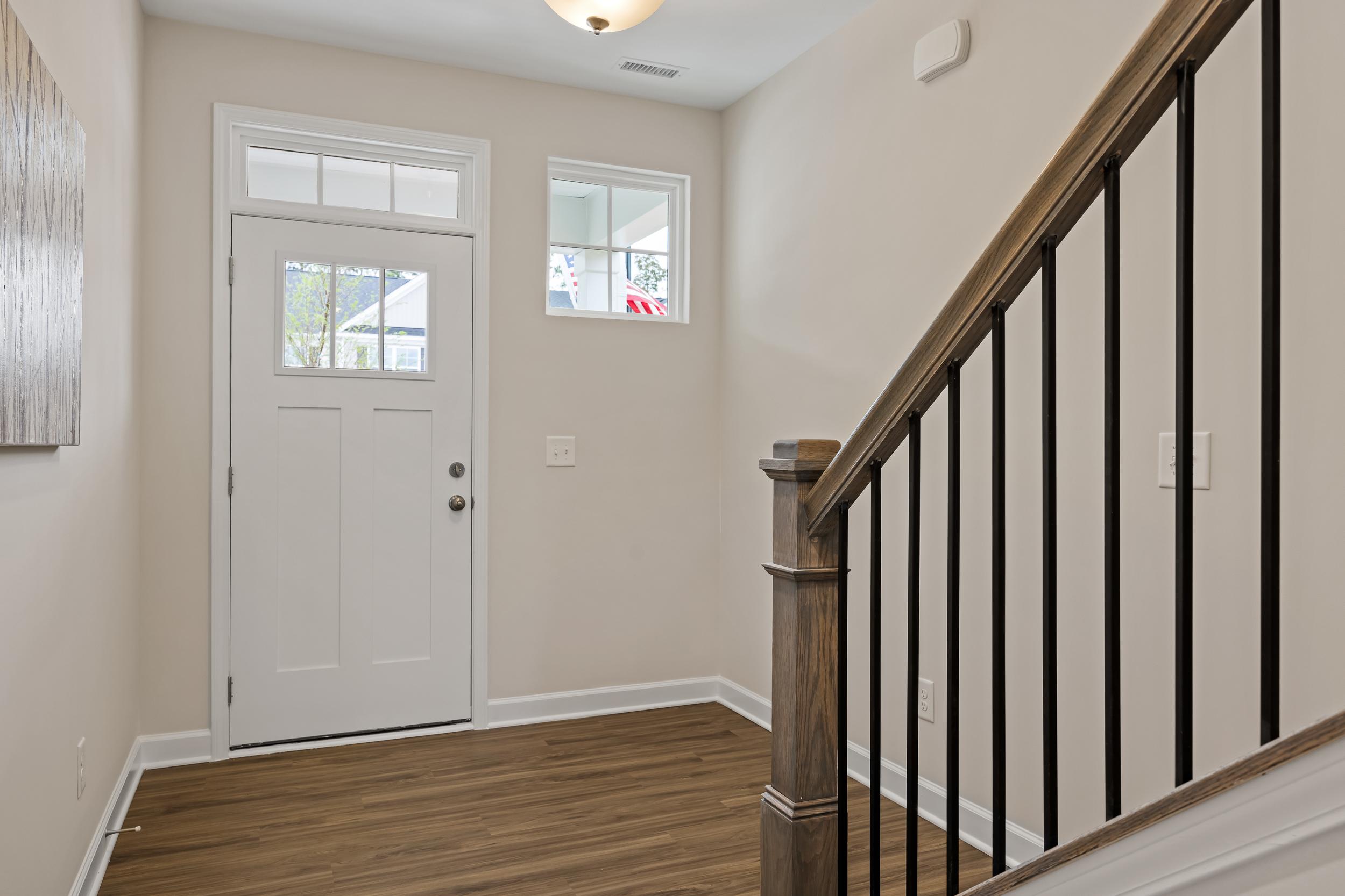Spacious entry foyer at Gregory Village in Lillington NC with white glass-paneled door, wooden stairs, black railings, and hardwood floors