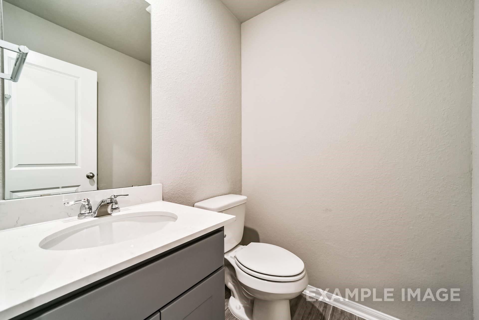 Modern half-bath with grey vanity, white countertop, and mirror in The Riviera A floor plan at Emberly in Beasley, Texas.