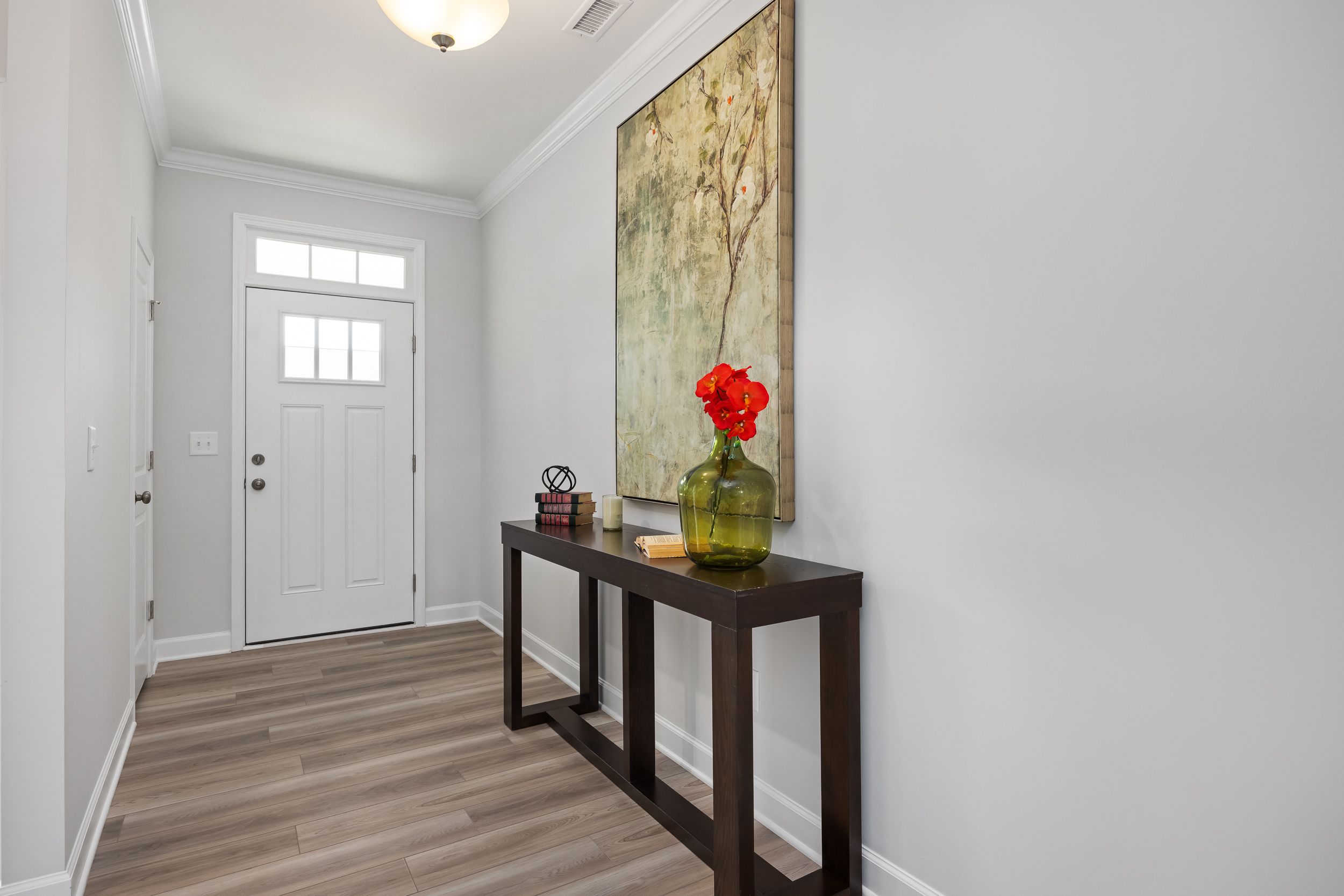 Spacious entry hall in The Daphne C home with gray walls, console table, red flower vase, and abstract art