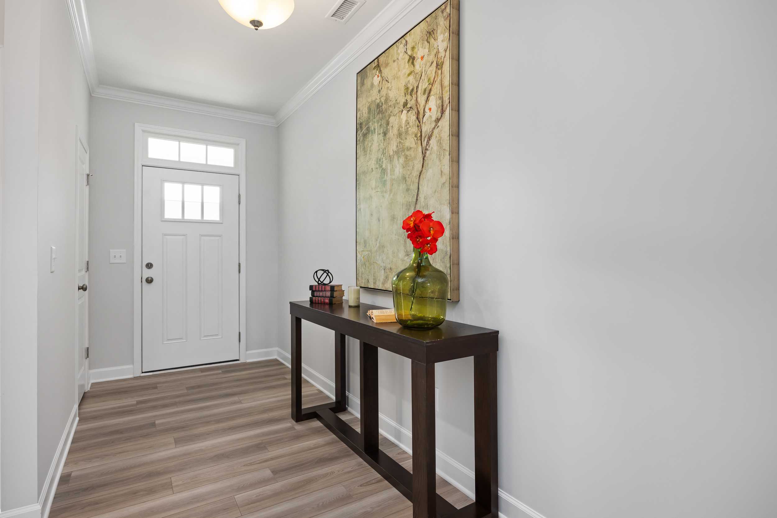 Spacious entry hall in The Daphne C home with gray walls, console table, red flower vase, and abstract art