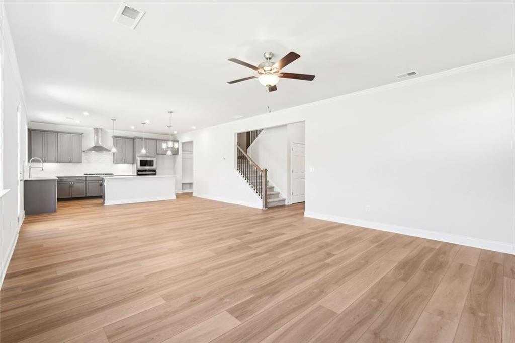 Open-concept kitchen and family room with gray cabinets, stainless appliances, hardwood floors, and staircase in The Hickory C, Hoschton, GA