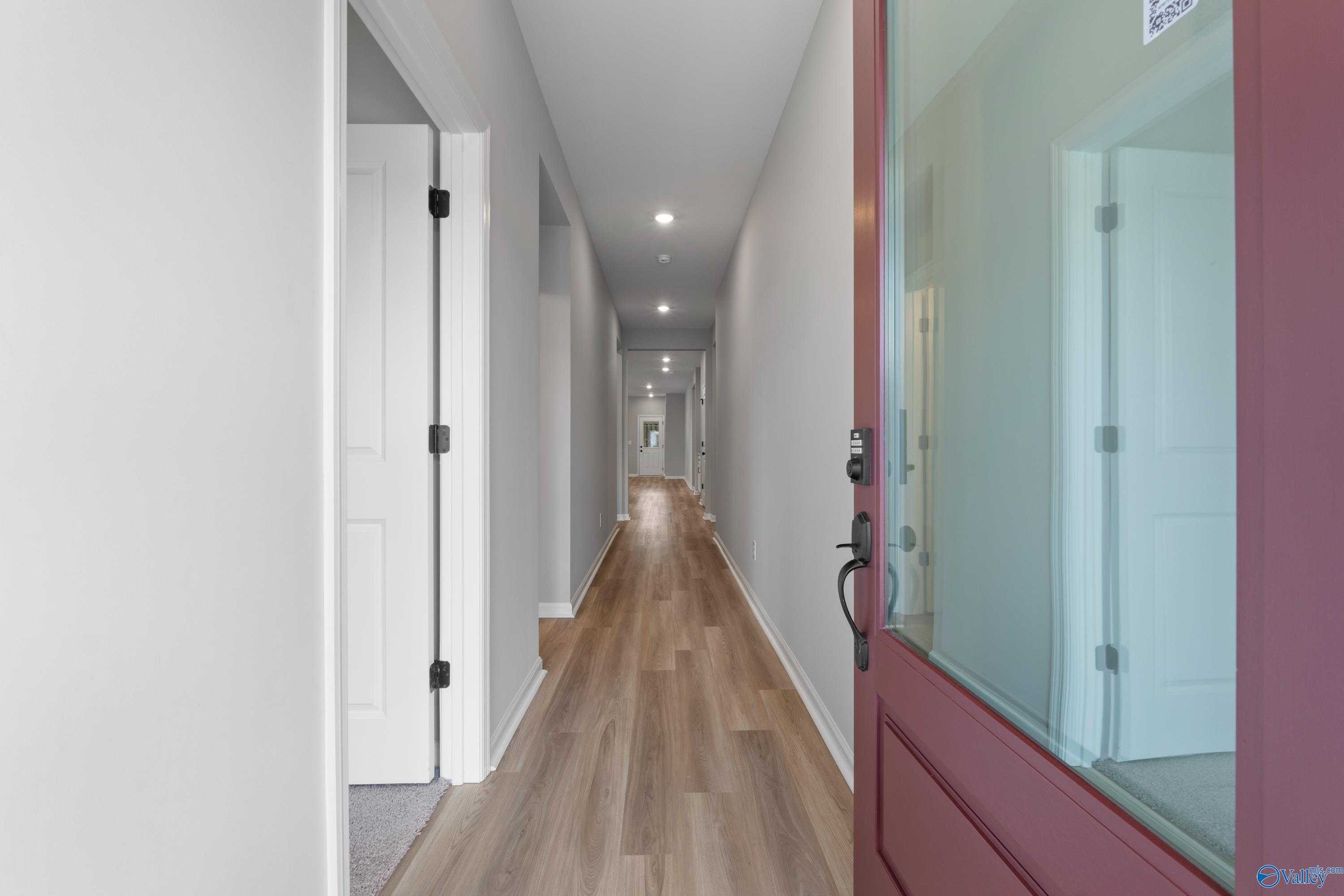 Bright hallway with light wood laminate floors, white walls, and red front door in Evermore Homes The Nantucket, Madison, Alabama