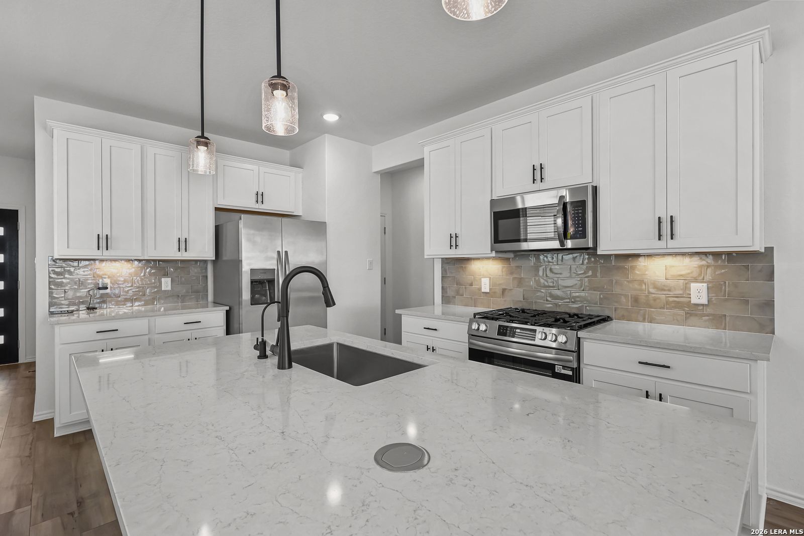 Modern kitchen with quartz island, white cabinets, and stainless appliances in The Gillian C home, Meadows at Oak Creek.