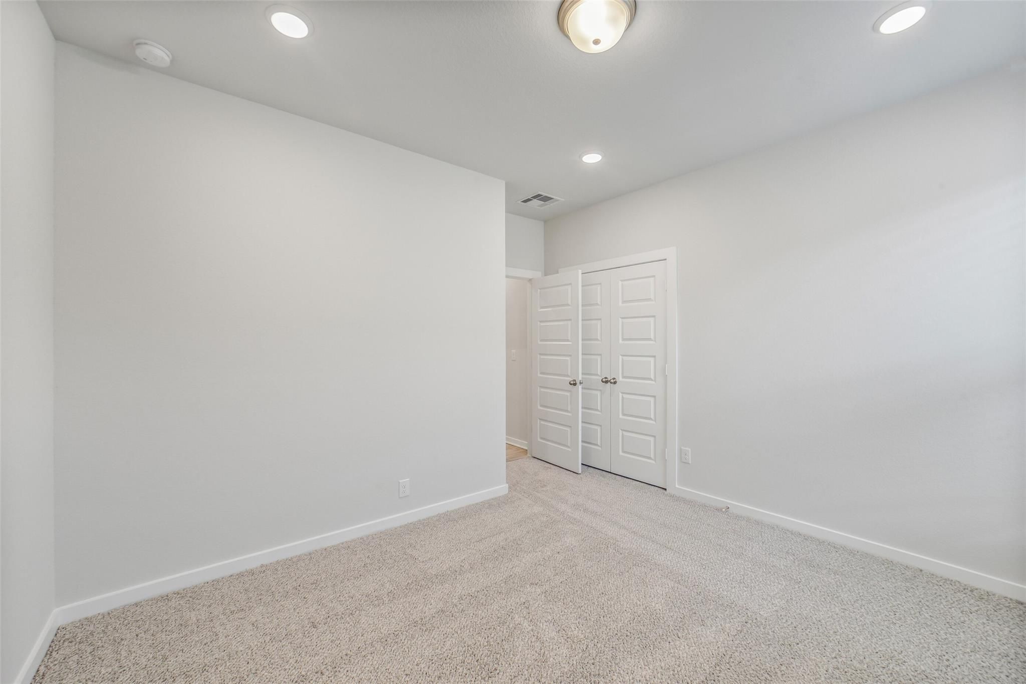 Bright bedroom with beige carpet, white walls, recessed lighting, and double closet doors in Davidson Homes The Acadia C, Magnolia, Texas