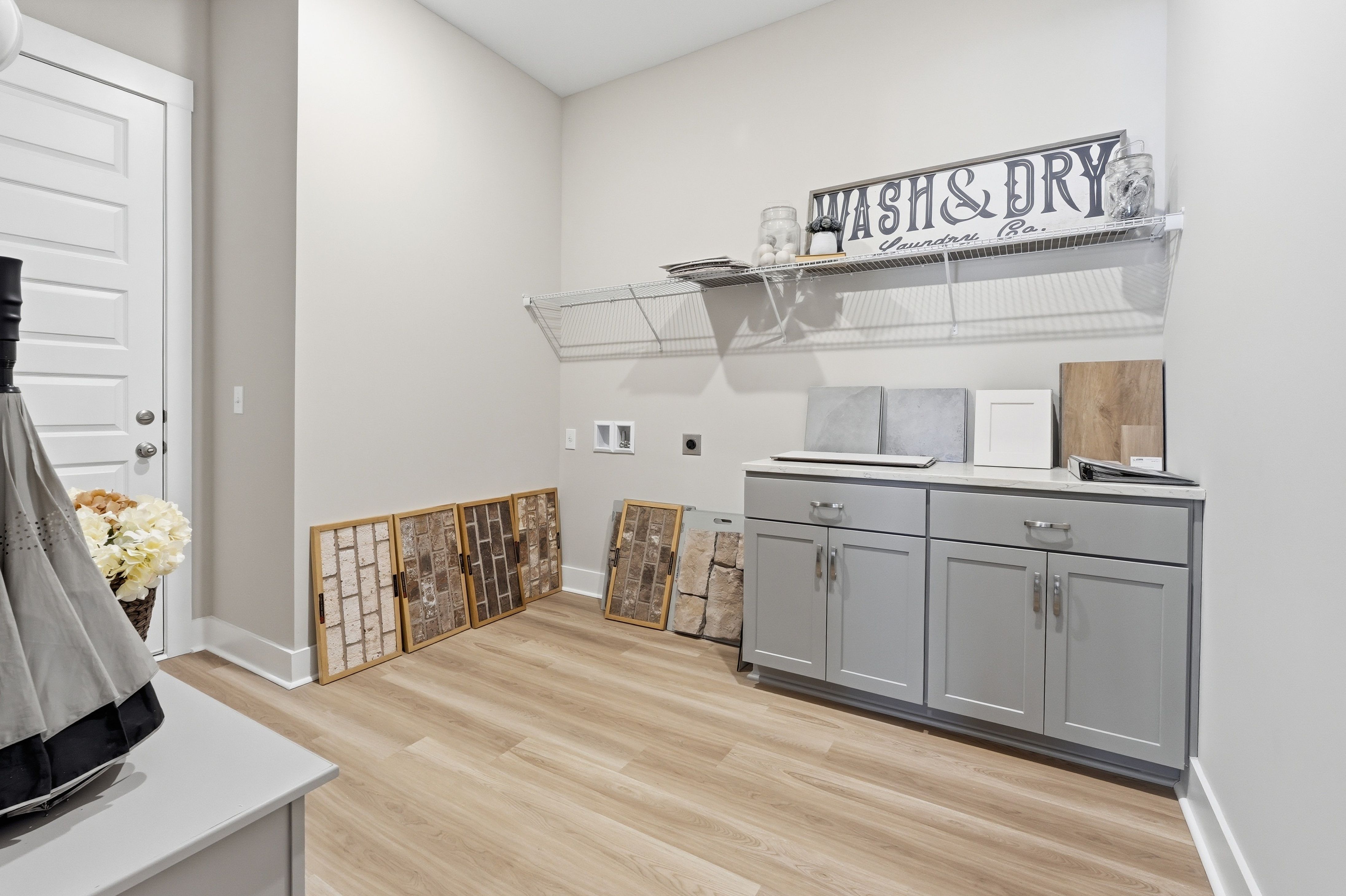 Spacious laundry room at The Meadows at Hampton Cove in Owens Cross Roads AL with gray cabinets, wood flooring, and sample displays