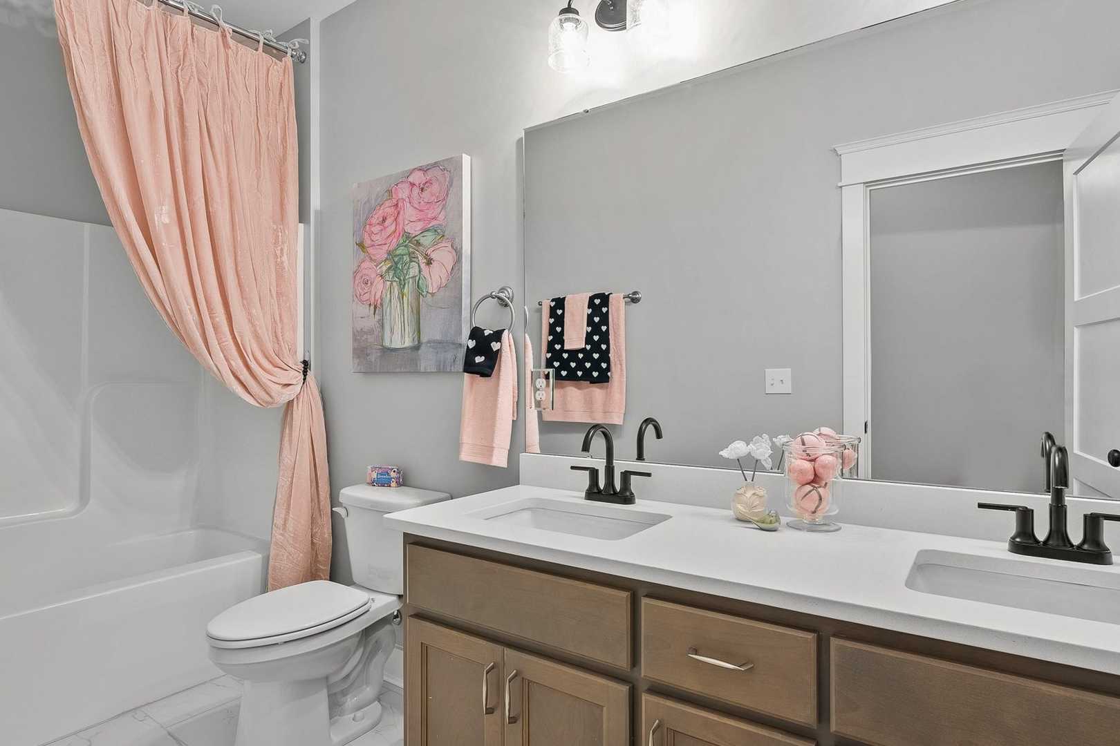 The Oxford master bathroom featuring double wood vanity, soaking tub with pink curtain, and floral accents