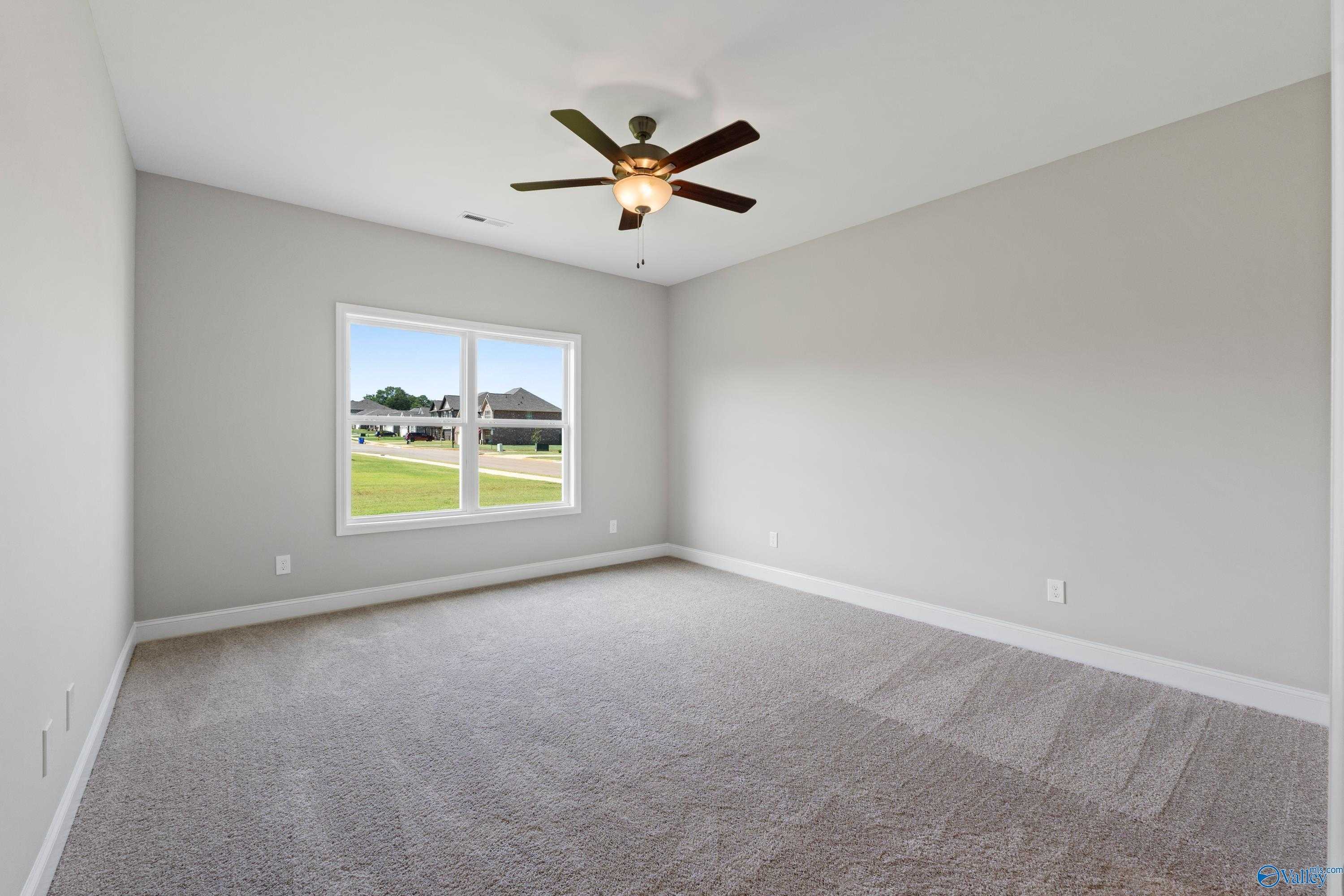 Bright secondary bedroom with ceiling fan, beige carpet, and window view of green lawn in Davidson Homes The Daphne C, Athens, Alabama