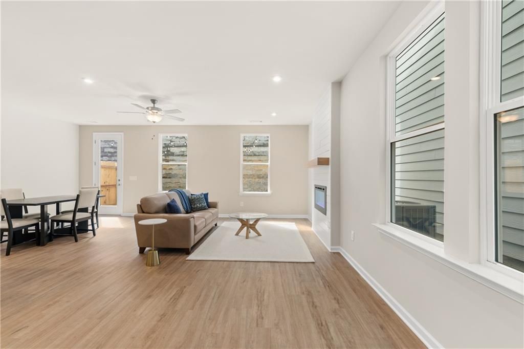 Cozy open living room with tan leather sofa, modern fireplace, dining table, hardwood floors, and large windows in The Marion B home, Kennesaw, GA