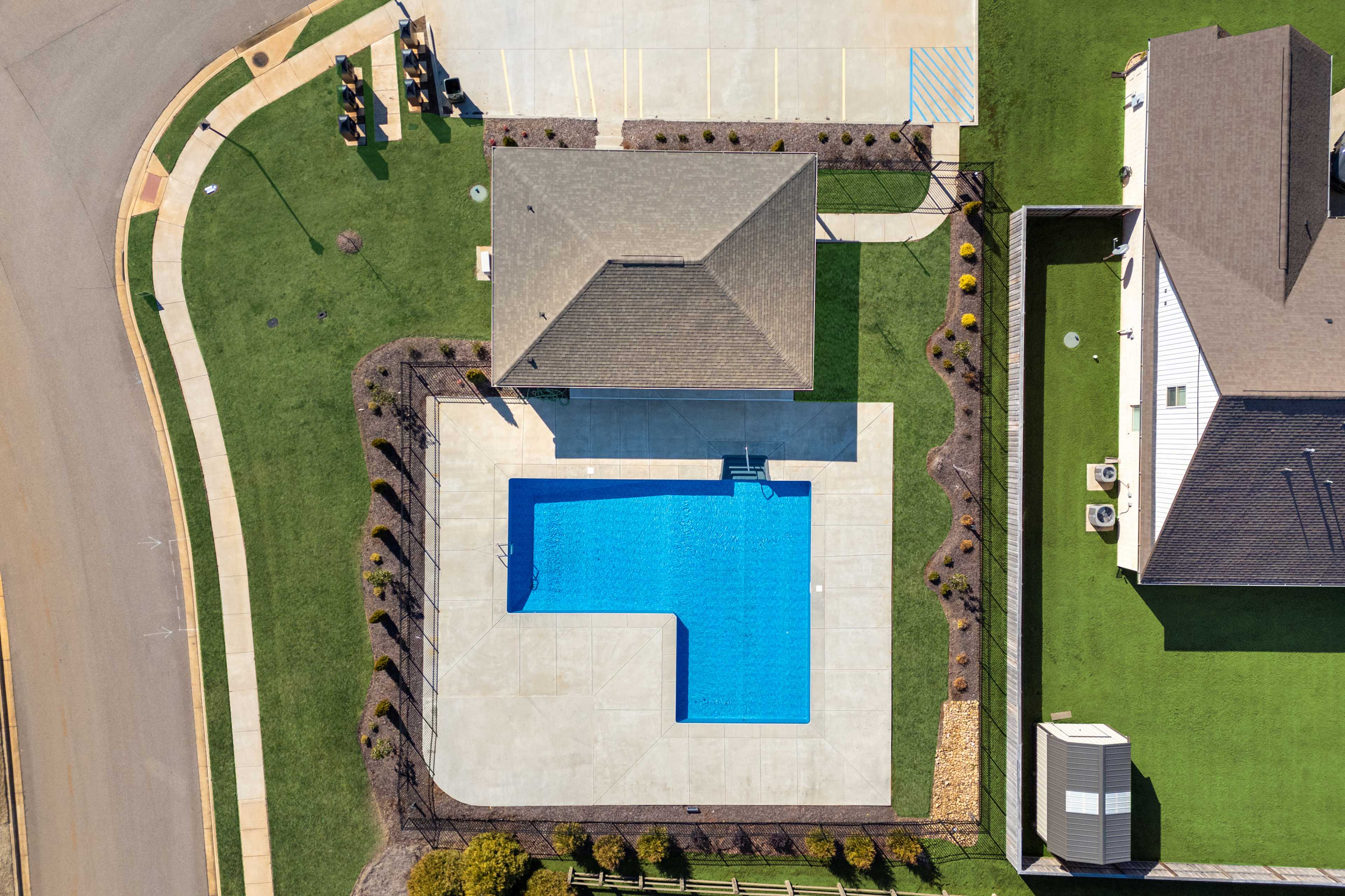 Aerial view of L-shaped blue swimming pool and clubhouse at Ivy Hills in Toney, Alabama with landscaped deck and greenery