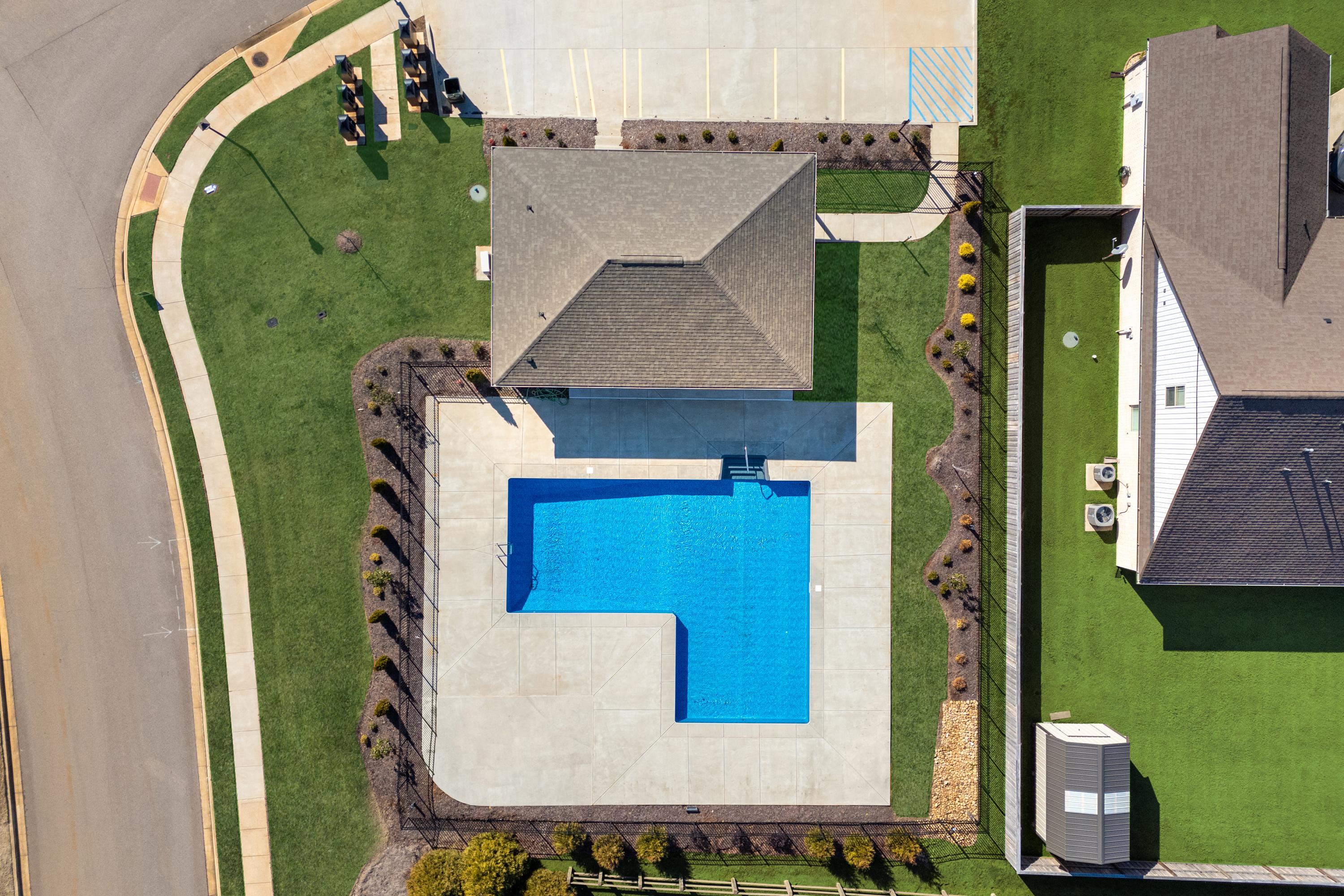 Aerial view of L-shaped blue swimming pool and clubhouse at Ivy Hills in Toney, Alabama with landscaped deck and greenery