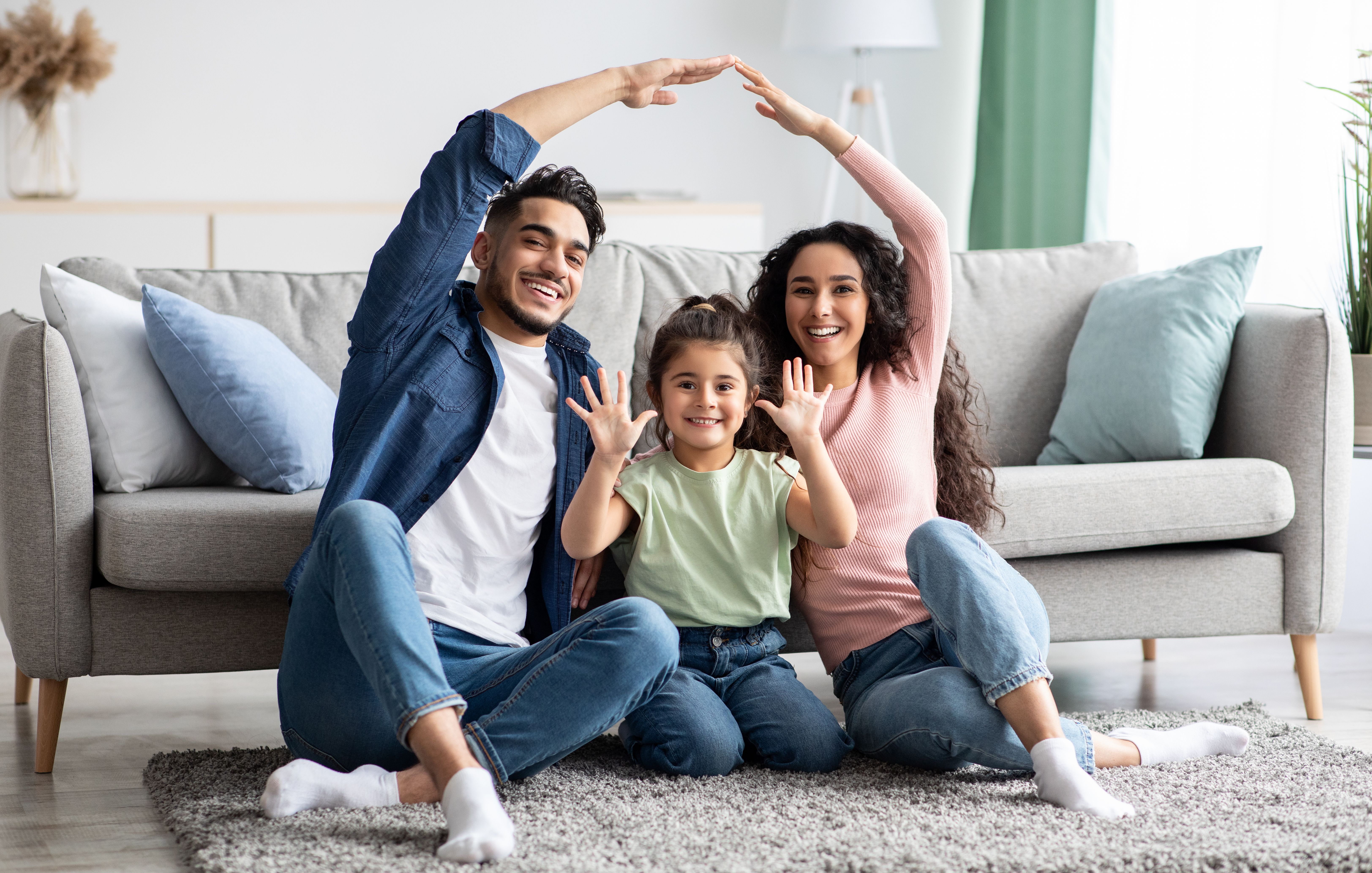 Happy family forming house shape with arms on gray sofa in modern Robins Landing living room, Houston Texas by Davidson Homes