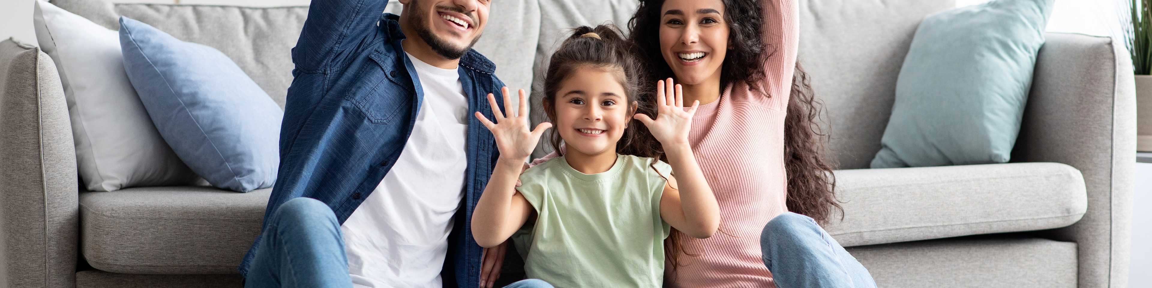 Happy family forming house shape with arms on gray sofa in modern Robins Landing living room, Houston Texas by Davidson Homes