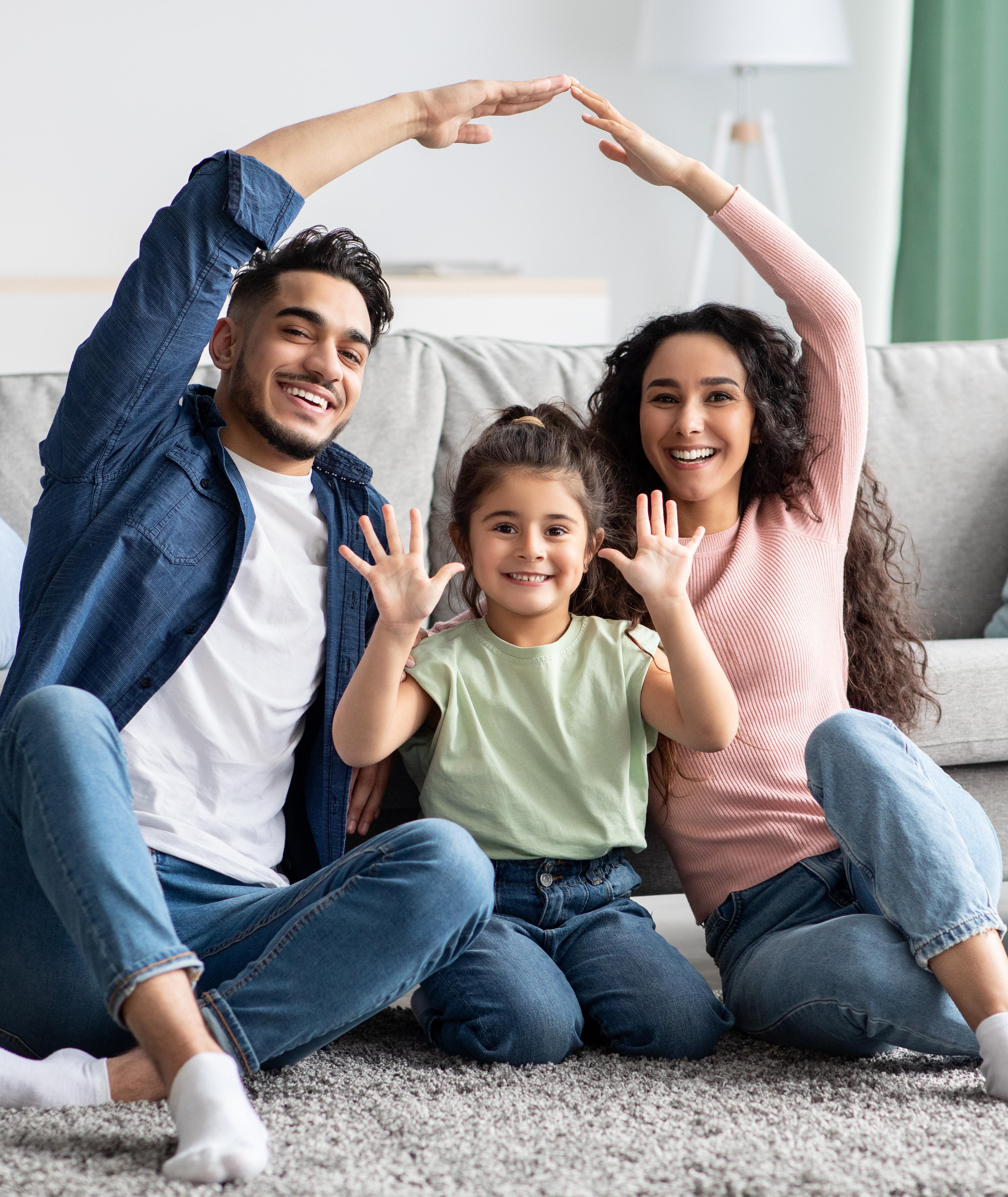 Happy family forming house shape with arms on gray sofa in modern Robins Landing living room, Houston Texas by Davidson Homes