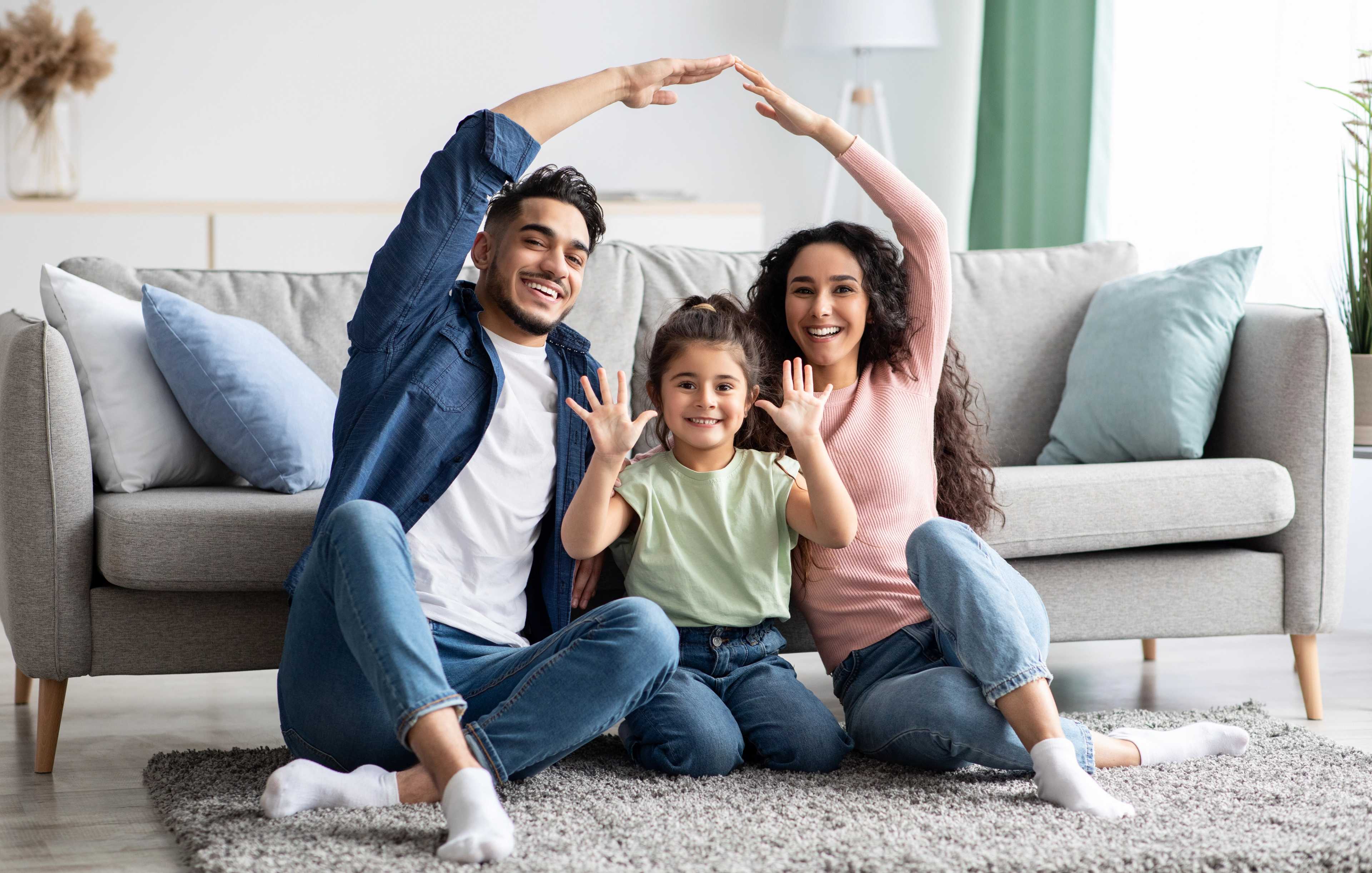 Happy family forming house shape with arms on gray sofa in modern Robins Landing living room, Houston Texas by Davidson Homes
