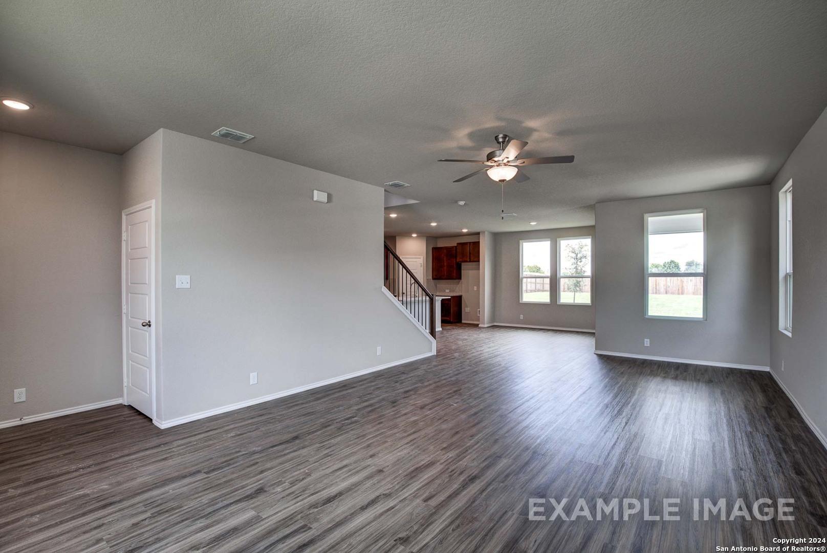 Expansive open living room with hardwood floors, ceiling fans, large windows, and staircase in Davidson Homes The Murray J, Bricewood, San Antonio