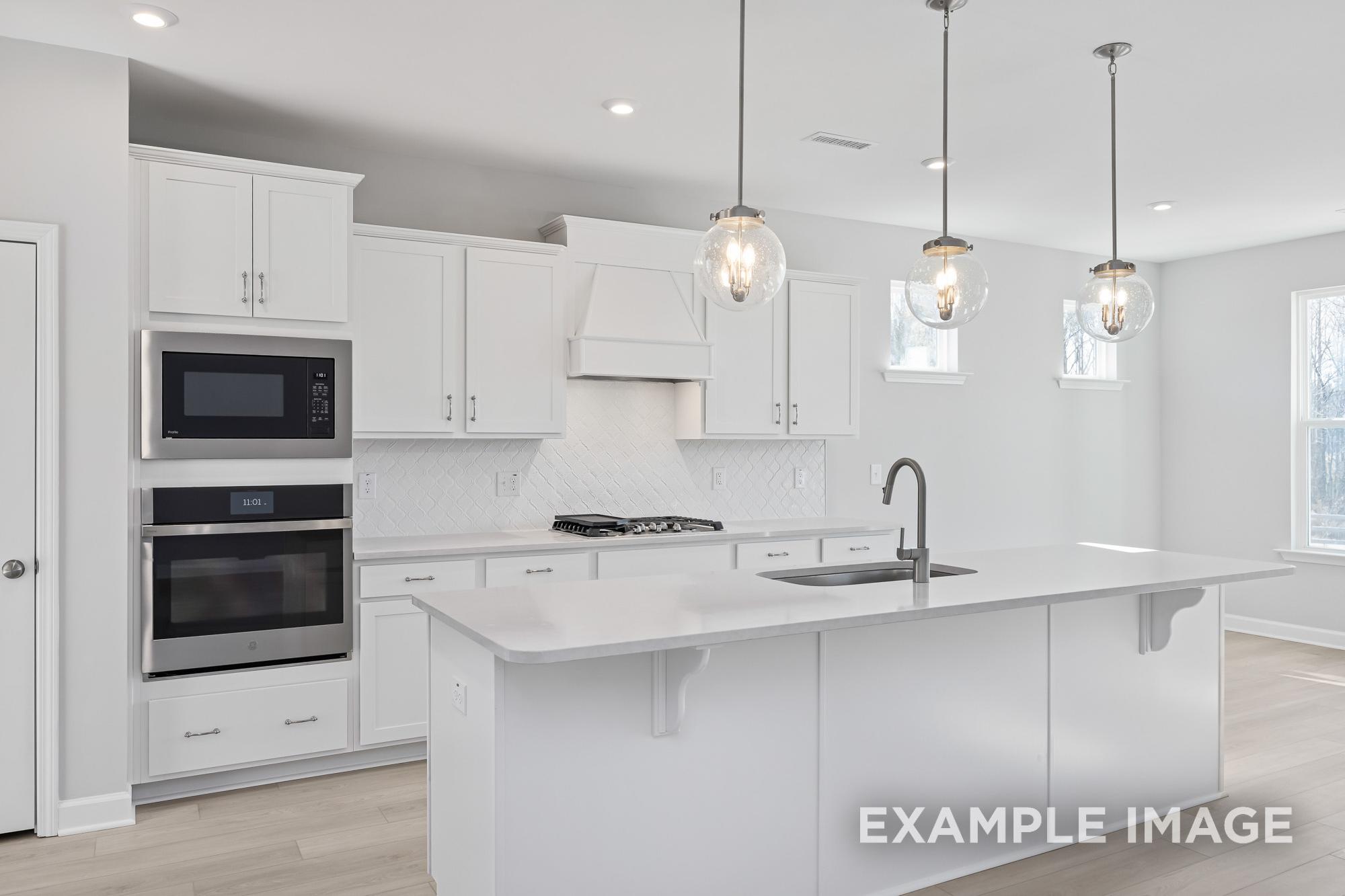Modern kitchen in The Cypress B II by Davidson Homes featuring white shaker cabinets, large island, double ovens, and pendant lights