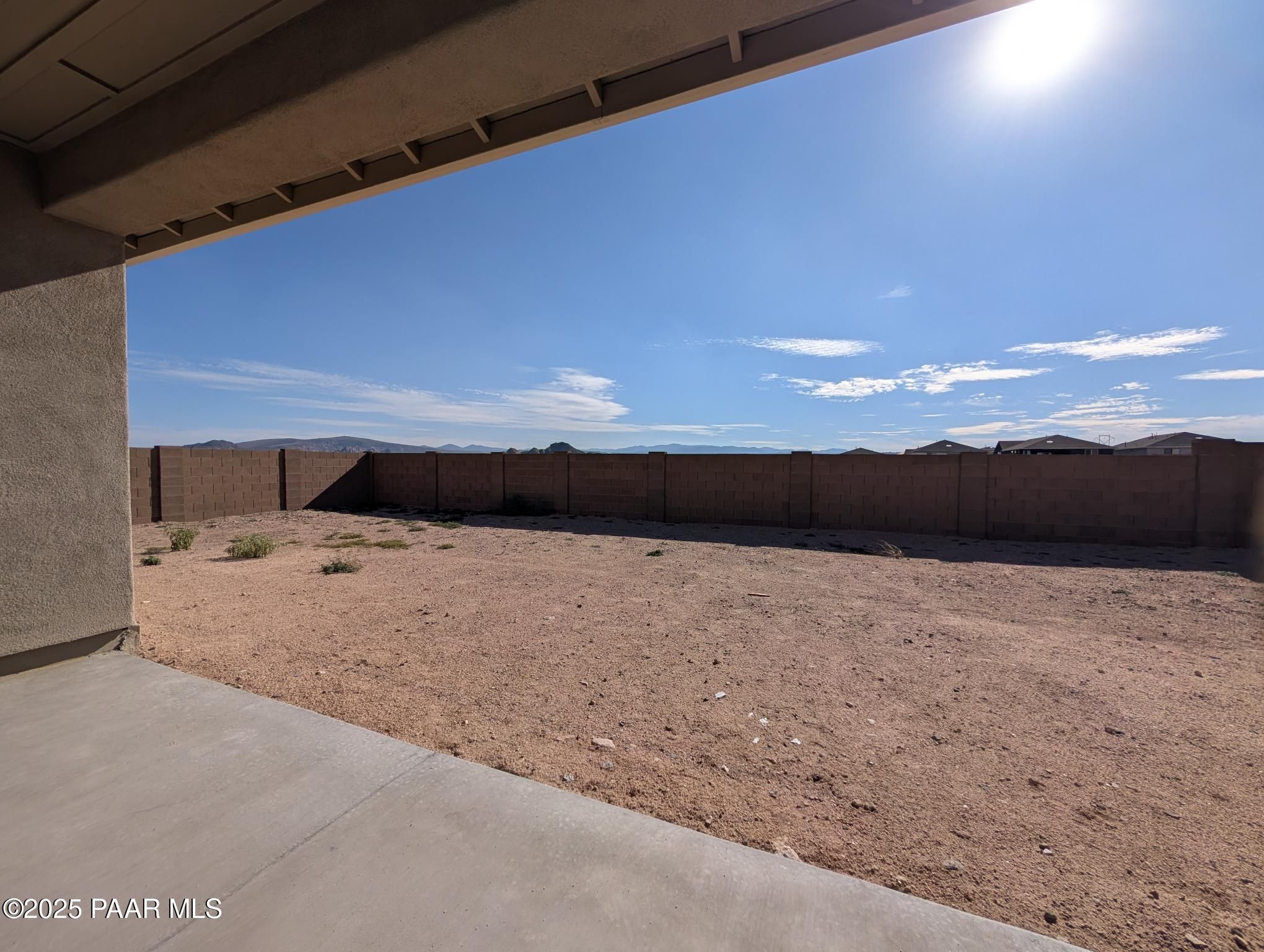 Spacious desert backyard with block wall fence and sparse vegetation from covered patio in The Sheridan II F home, Prescott, Arizona