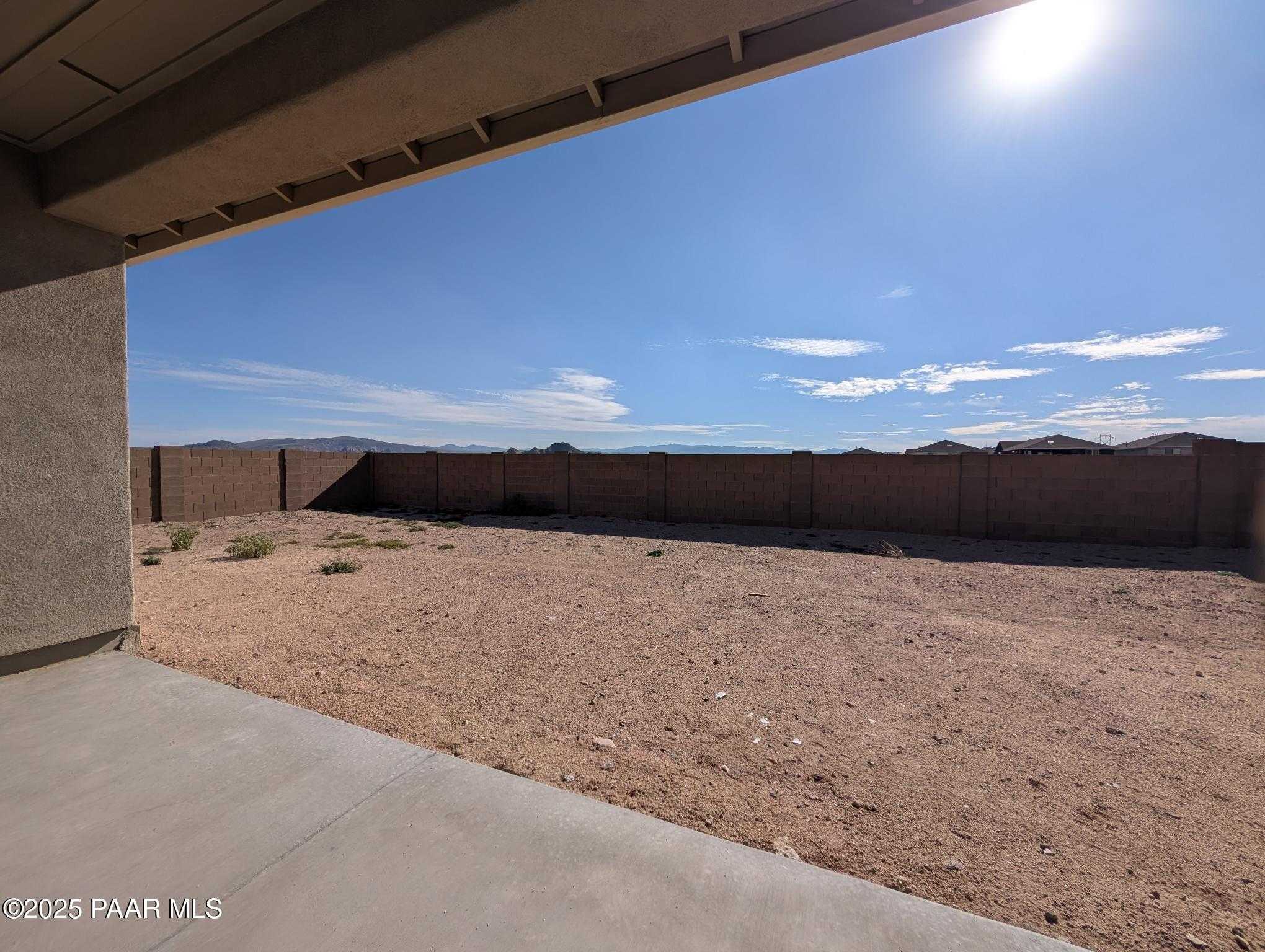 Spacious desert backyard with block wall fence and sparse vegetation from covered patio in The Sheridan II F home, Prescott, Arizona