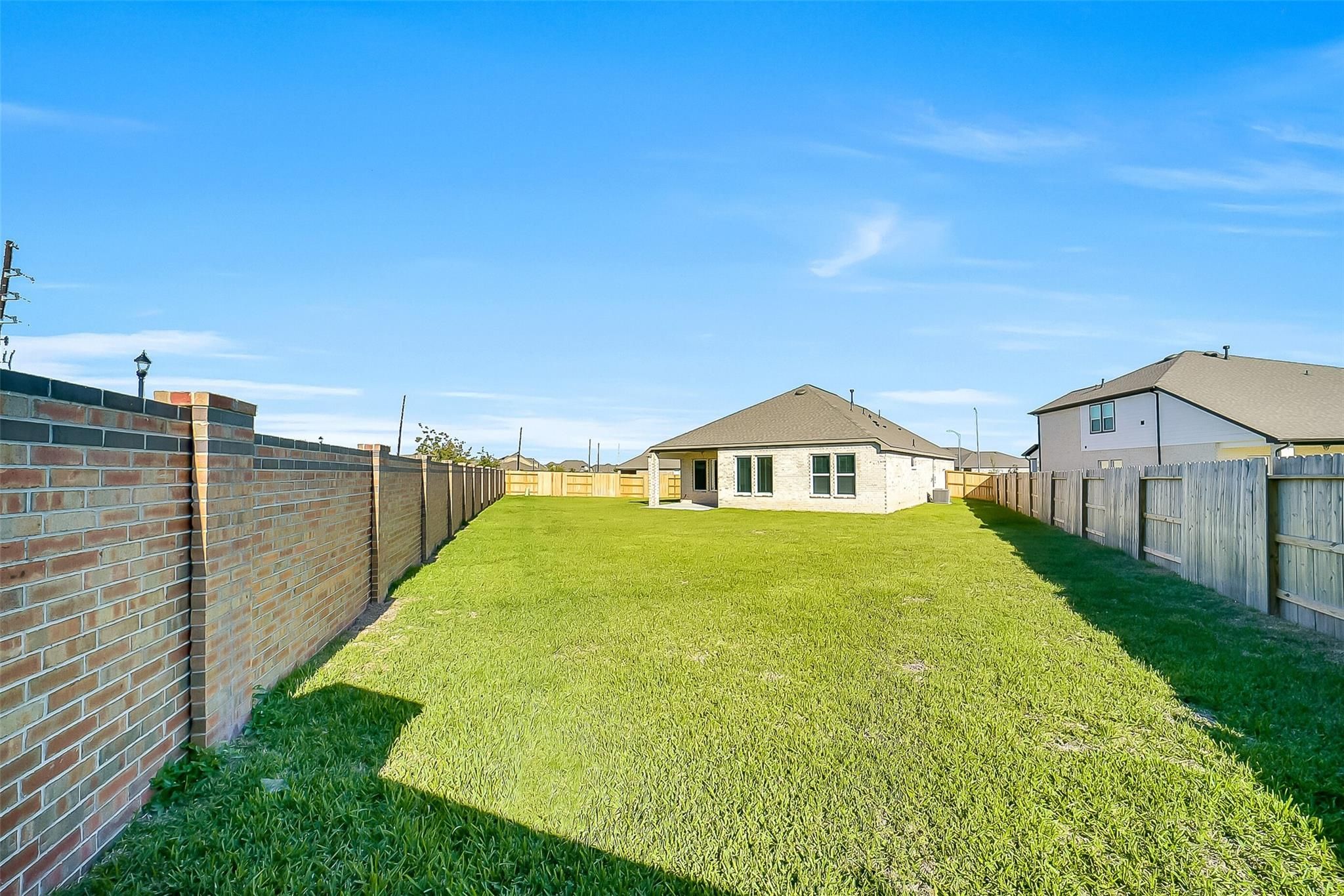 Private fenced backyard with lush green lawn, covered patio, and beige single-story home in Davidson Homes The Acadia A, Sunterra, Katy, Texas
