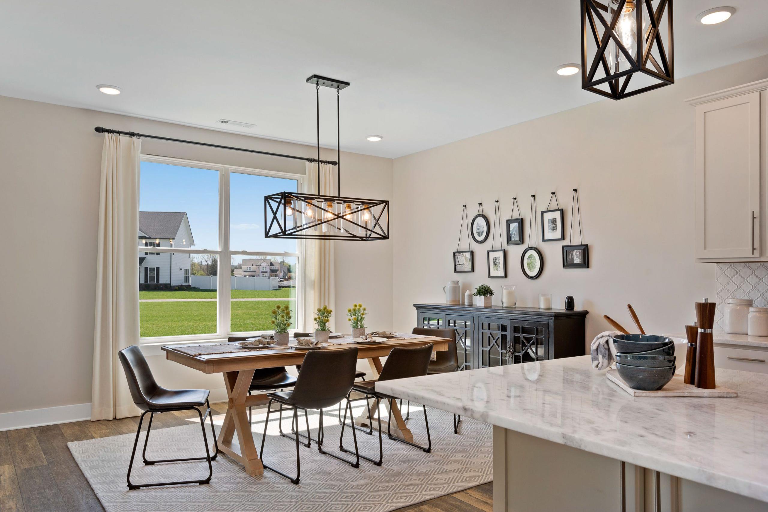 Open-concept dining room at Rivers Edge Murfreesboro TN by Davidson Homes with wooden table, black chandelier, and window view of green field
