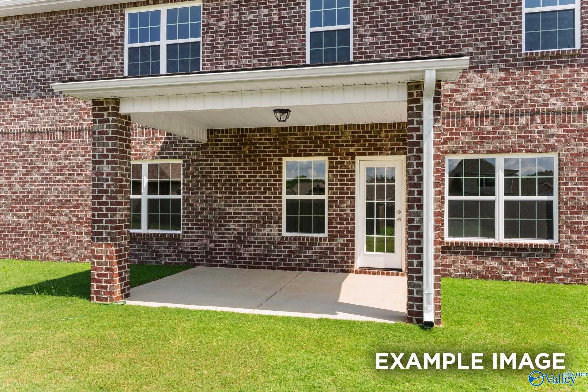 Covered back patio with brick accents, French doors, and green lawn in Davidson Homes The Madison A, Creekside, Harvest, Alabama