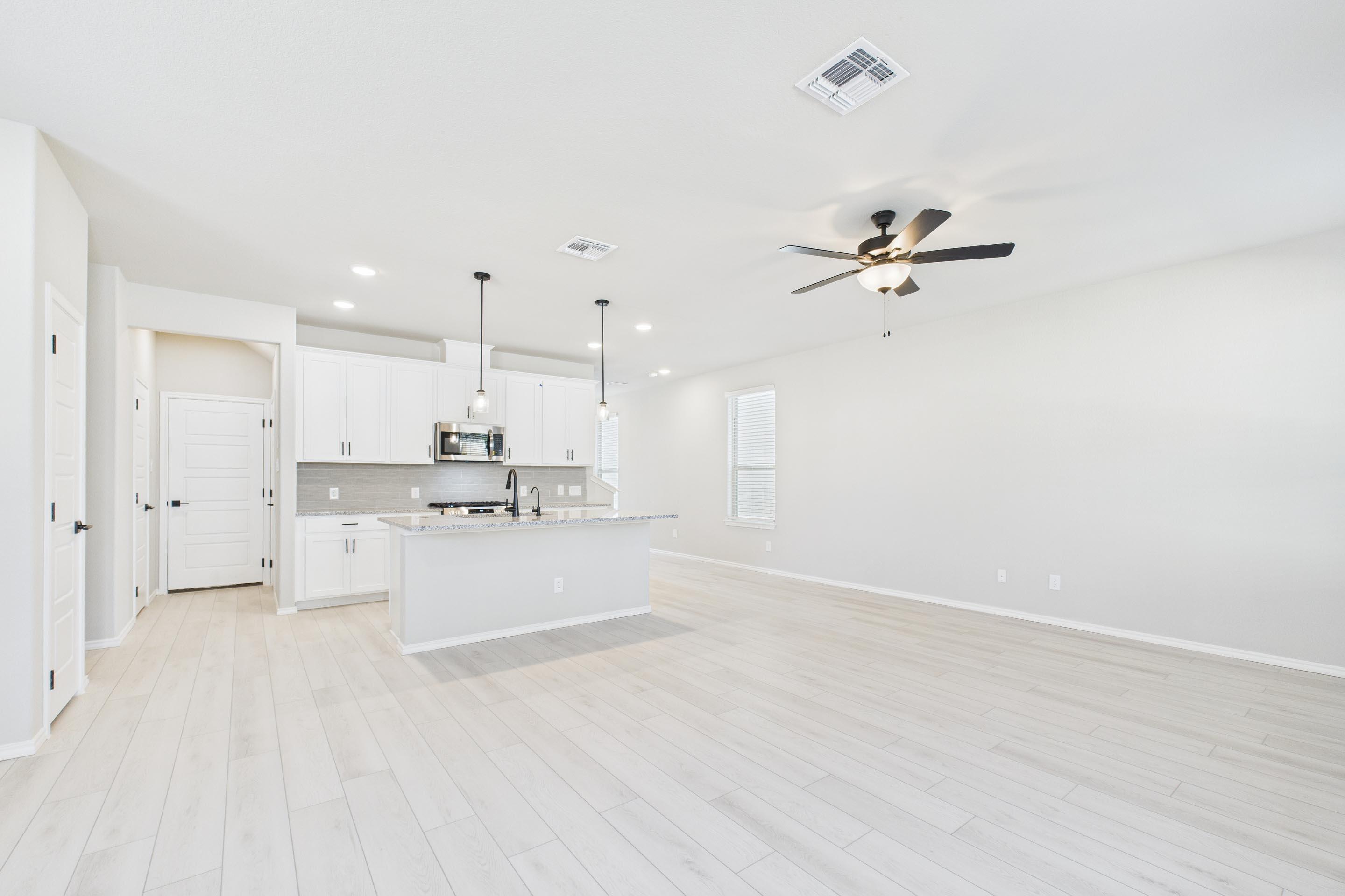 Open-concept kitchen and living area in The Charlotte floor plan featuring white cabinetry, island, and light wood flooring.