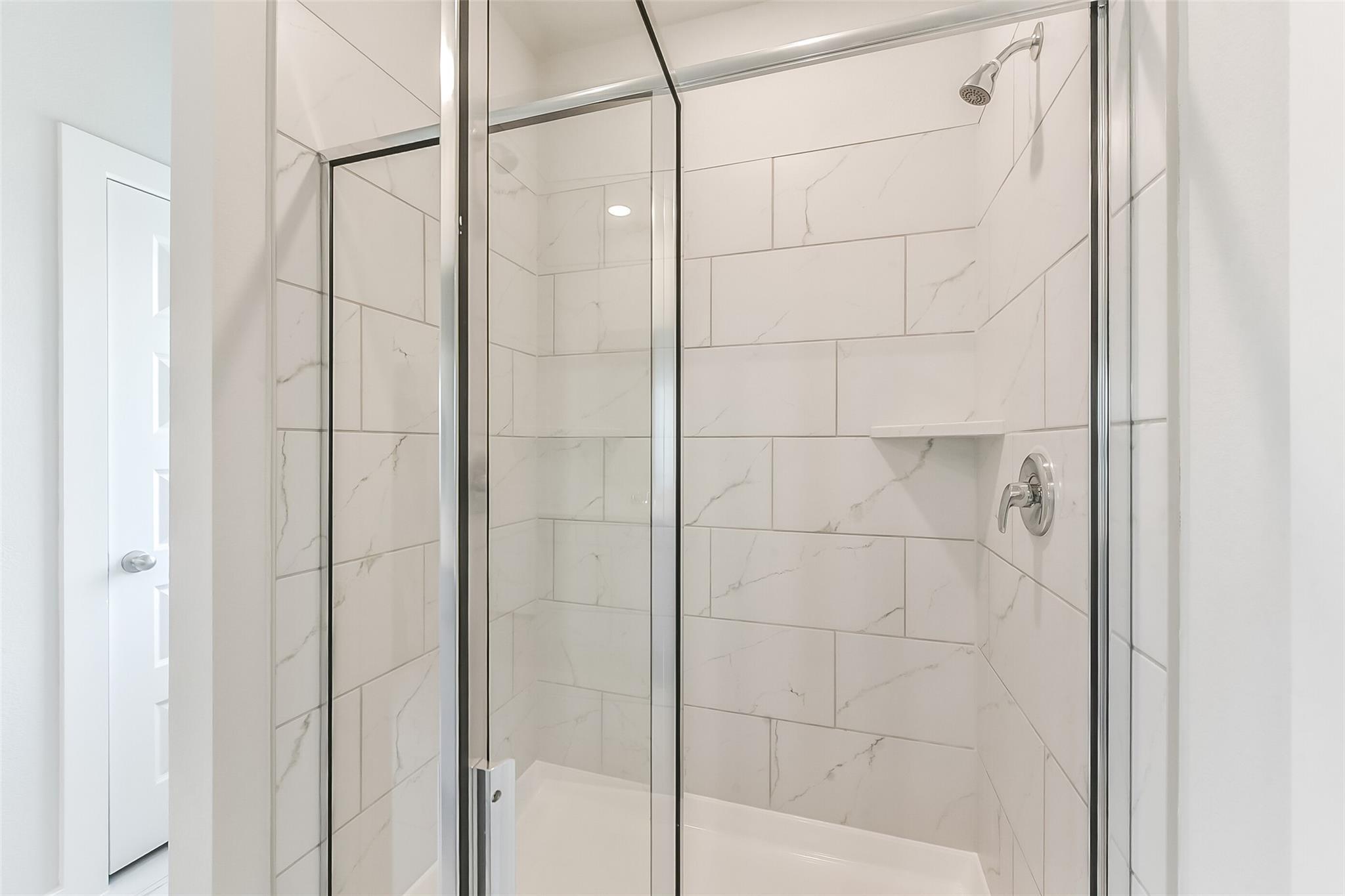 Elegant frameless glass shower with white marble subway tiles, rainfall head and niche in Davidson Homes The Tierra C bathroom, Dayton, Texas