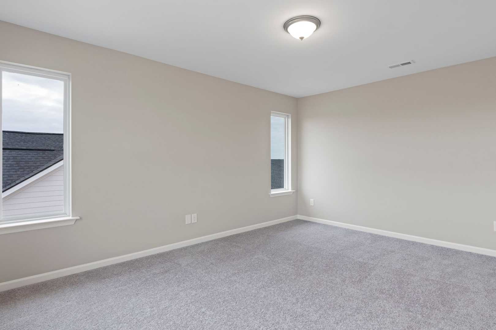 Spacious empty bedroom in The Stella by Evermore Homes, beige walls, gray carpet, large window overlooking roof