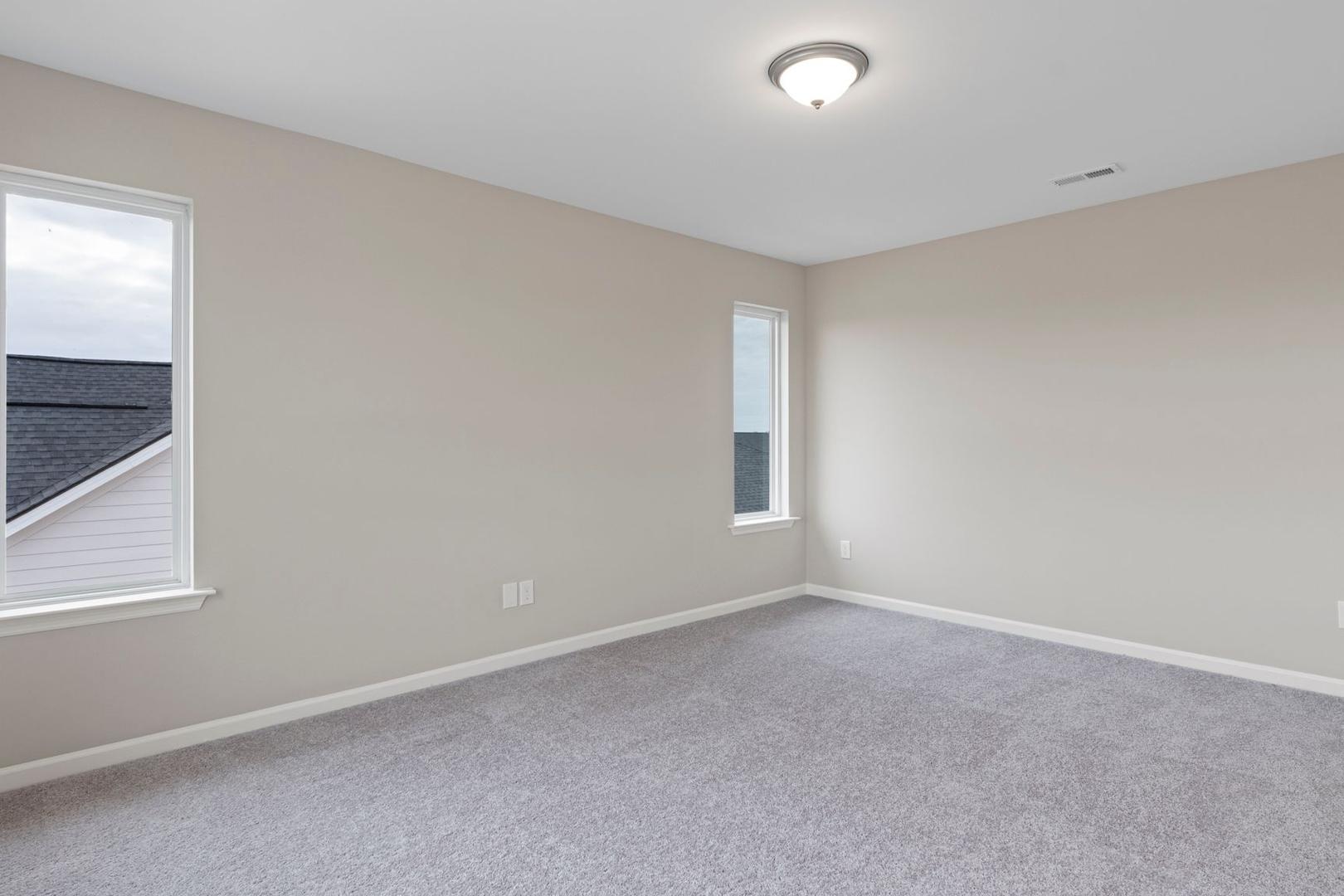 Spacious empty bedroom in The Stella A by Davidson Homes, featuring beige walls, gray carpet, large windows, and ceiling light