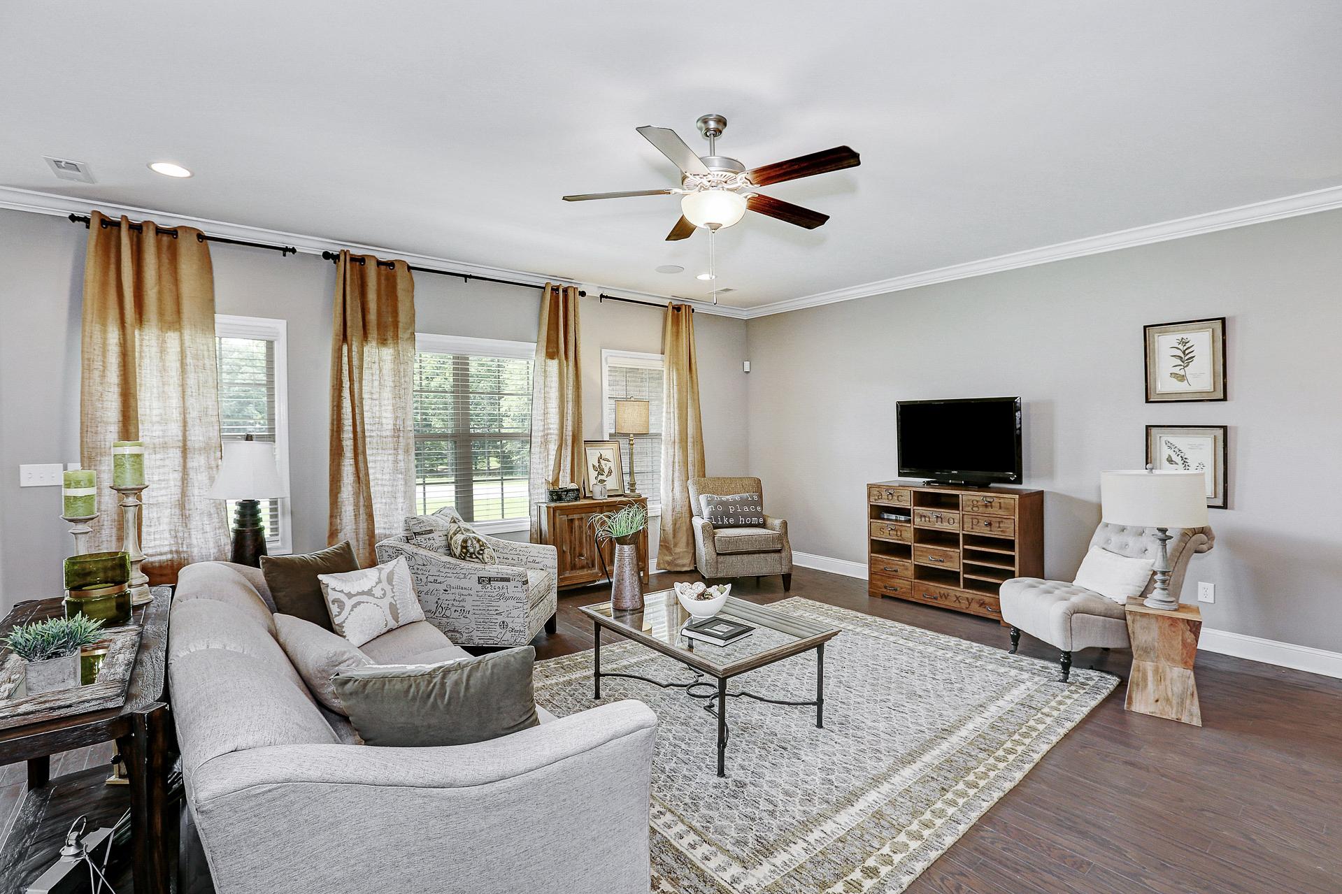 Spacious living room at Stone Creek Phase II in Cullman Alabama with gray sectional sofa, hardwood floors, large windows, and ceiling fan