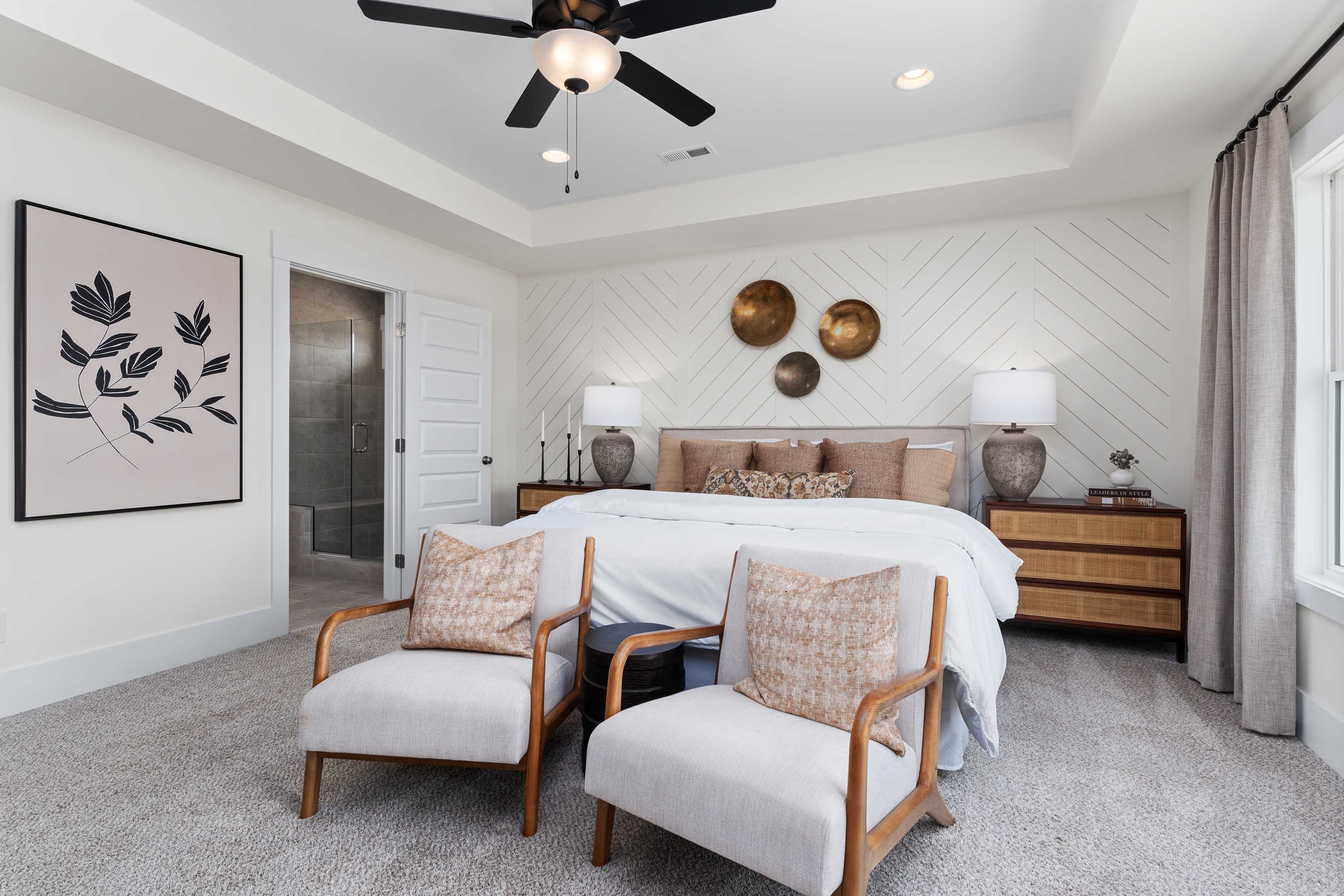 Spacious master bedroom in The Shelby A featuring king bed, armchairs, ceiling fan, shiplap walls, and abstract art