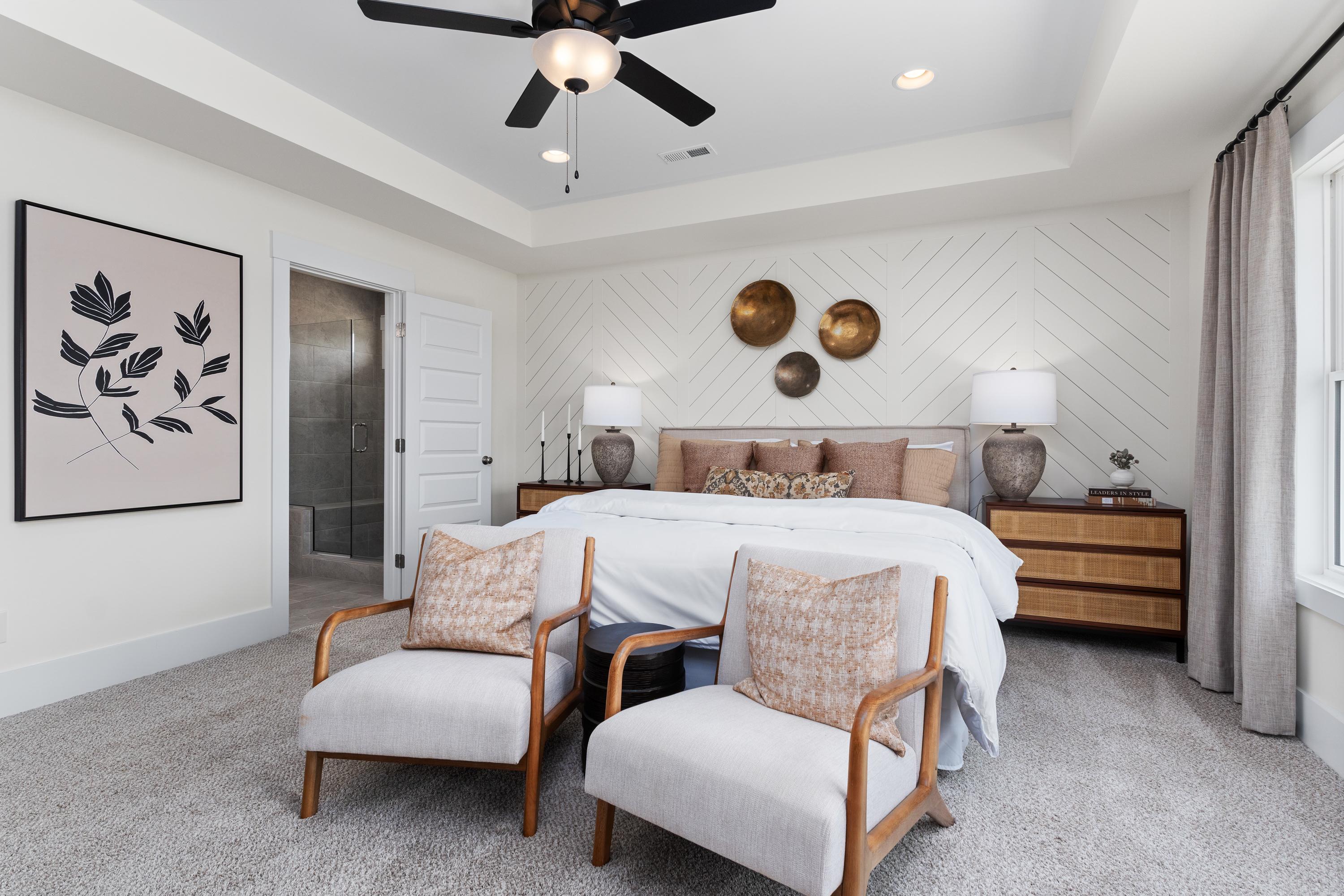 Spacious master bedroom in The Shelby A featuring king bed, armchairs, ceiling fan, shiplap walls, and abstract art