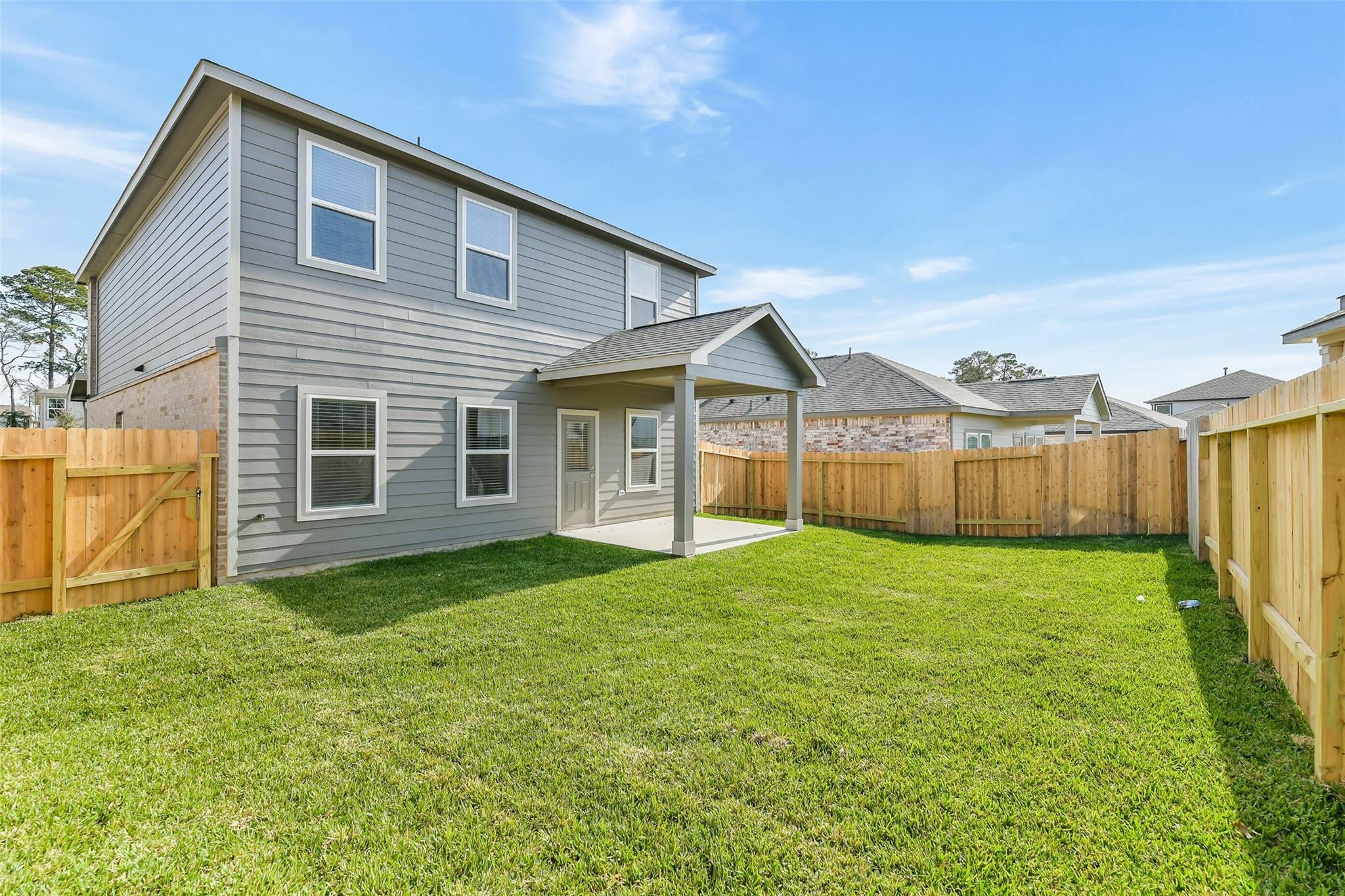 Two-story gray Davidson Homes Trinity F with covered back patio, wooden fence, and lush green yard in Lakes at Black Oak, Magnolia, Texas