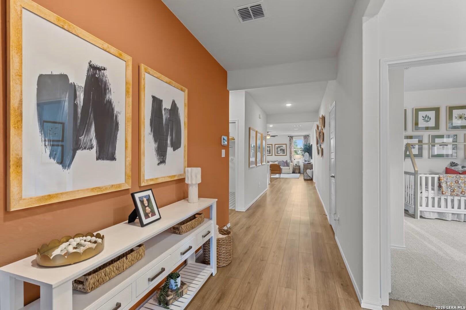 Elegant hallway with orange accent wall, abstract gold-framed art, white console table, leading to nursery in Davidson Homes The Daphne K, San Antonio