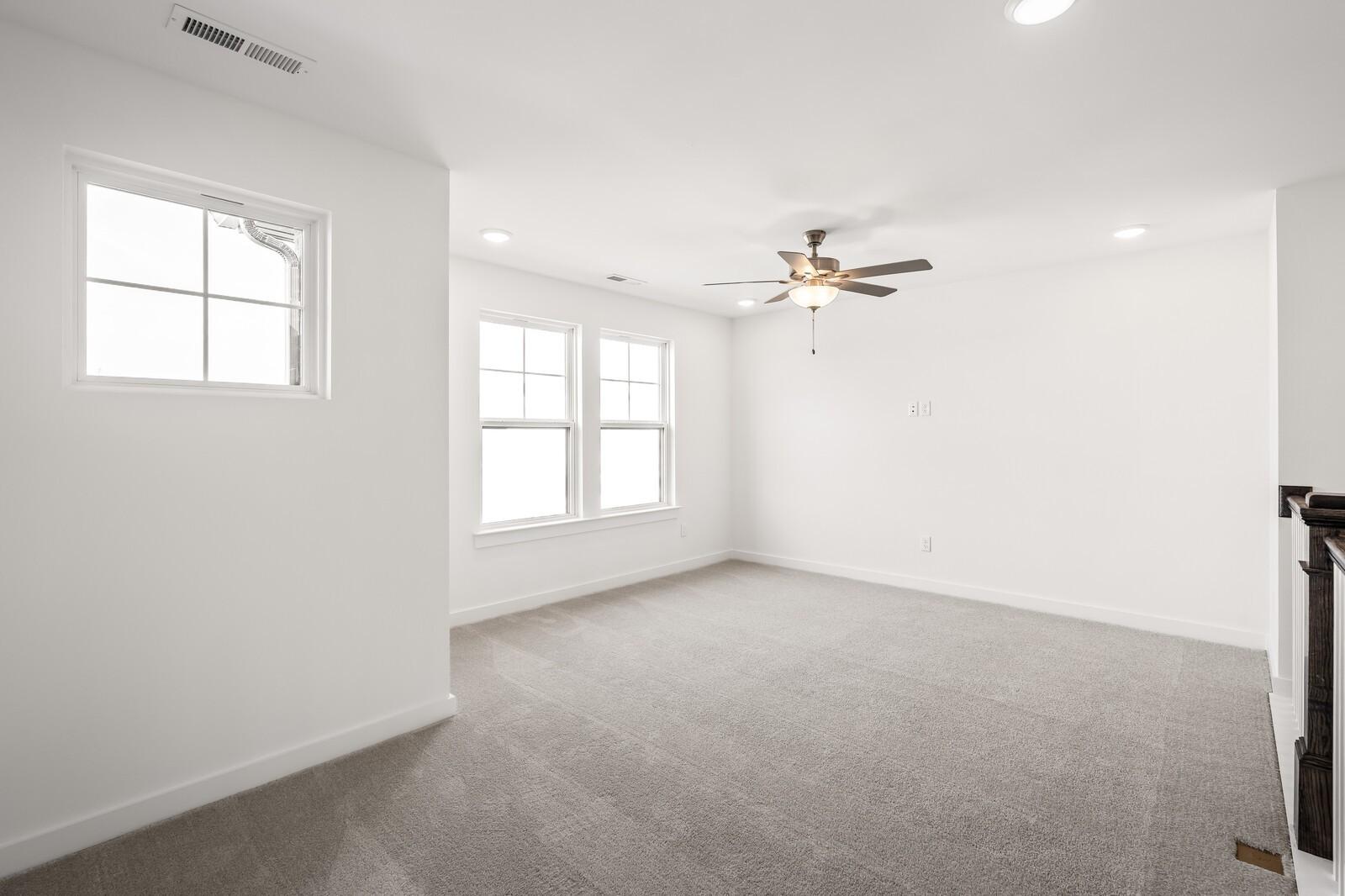 Bright upstairs loft with gray carpet, large double windows, bronze ceiling fan, and balcony railing in Davidson Homes Willow D, Mt. Juliet